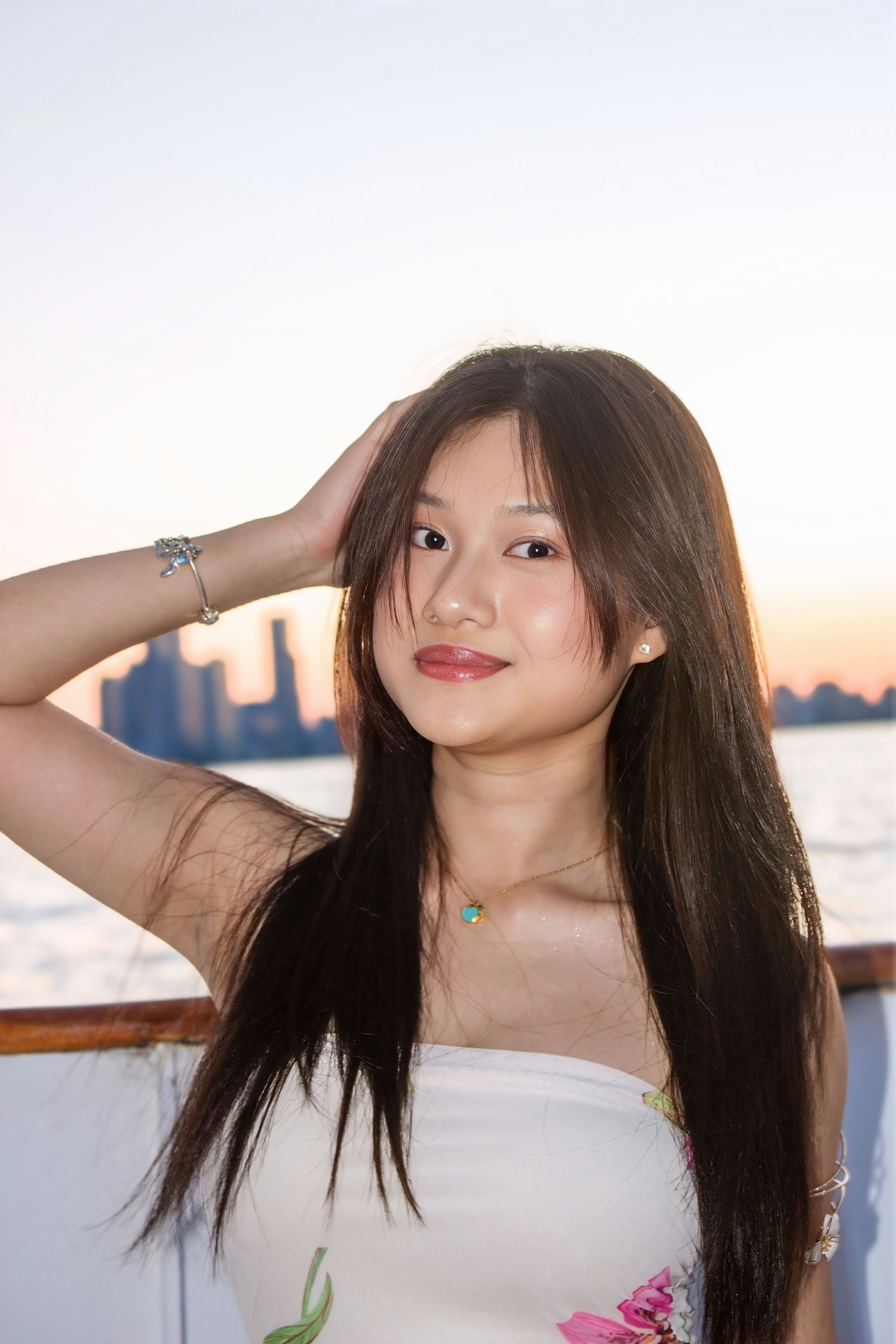 A woman with long dark hair posing on a boat against a city skyline