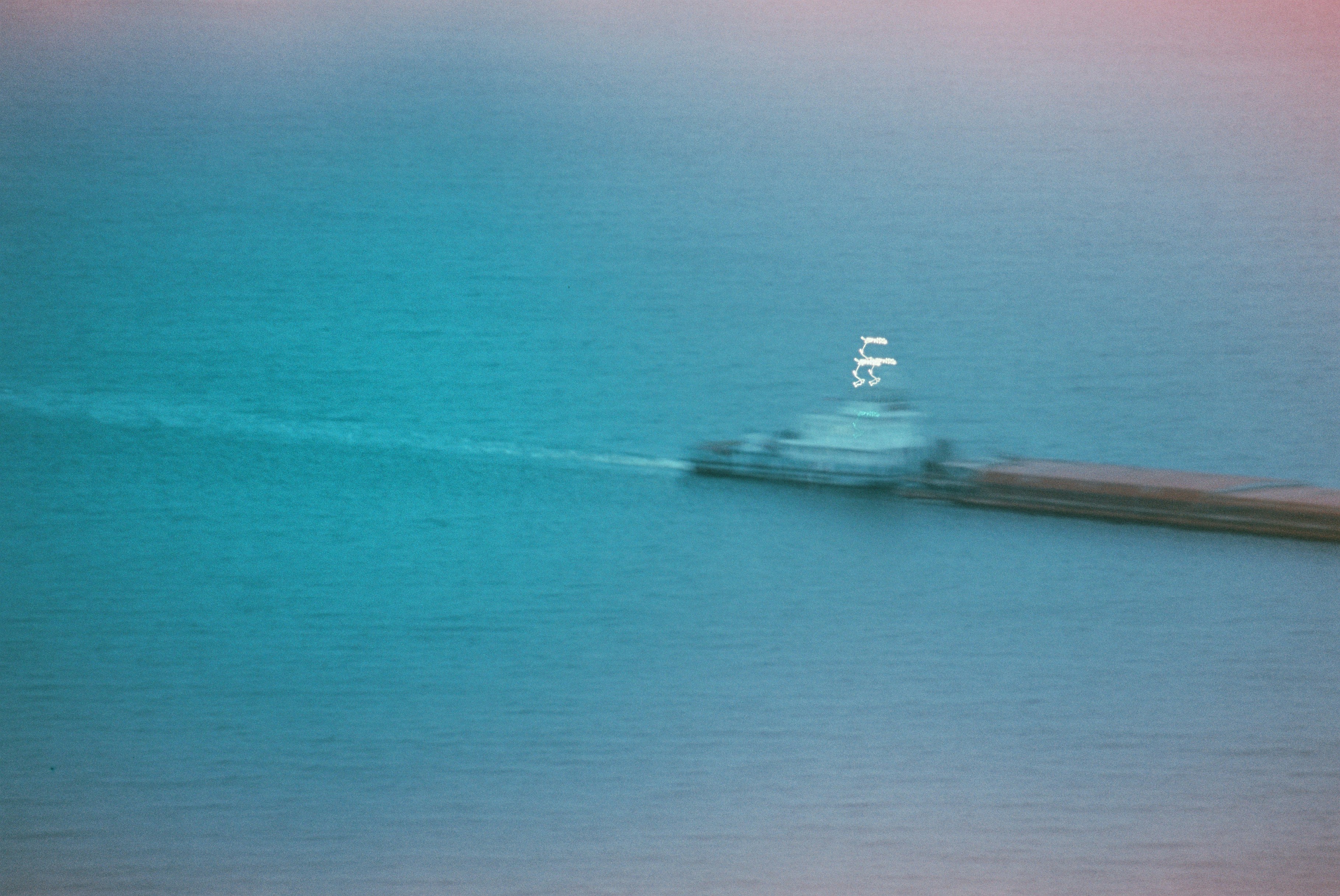 Ein Lastkahn, der über blaues Wasser fährt und eine weiße Spur hinterlässt.