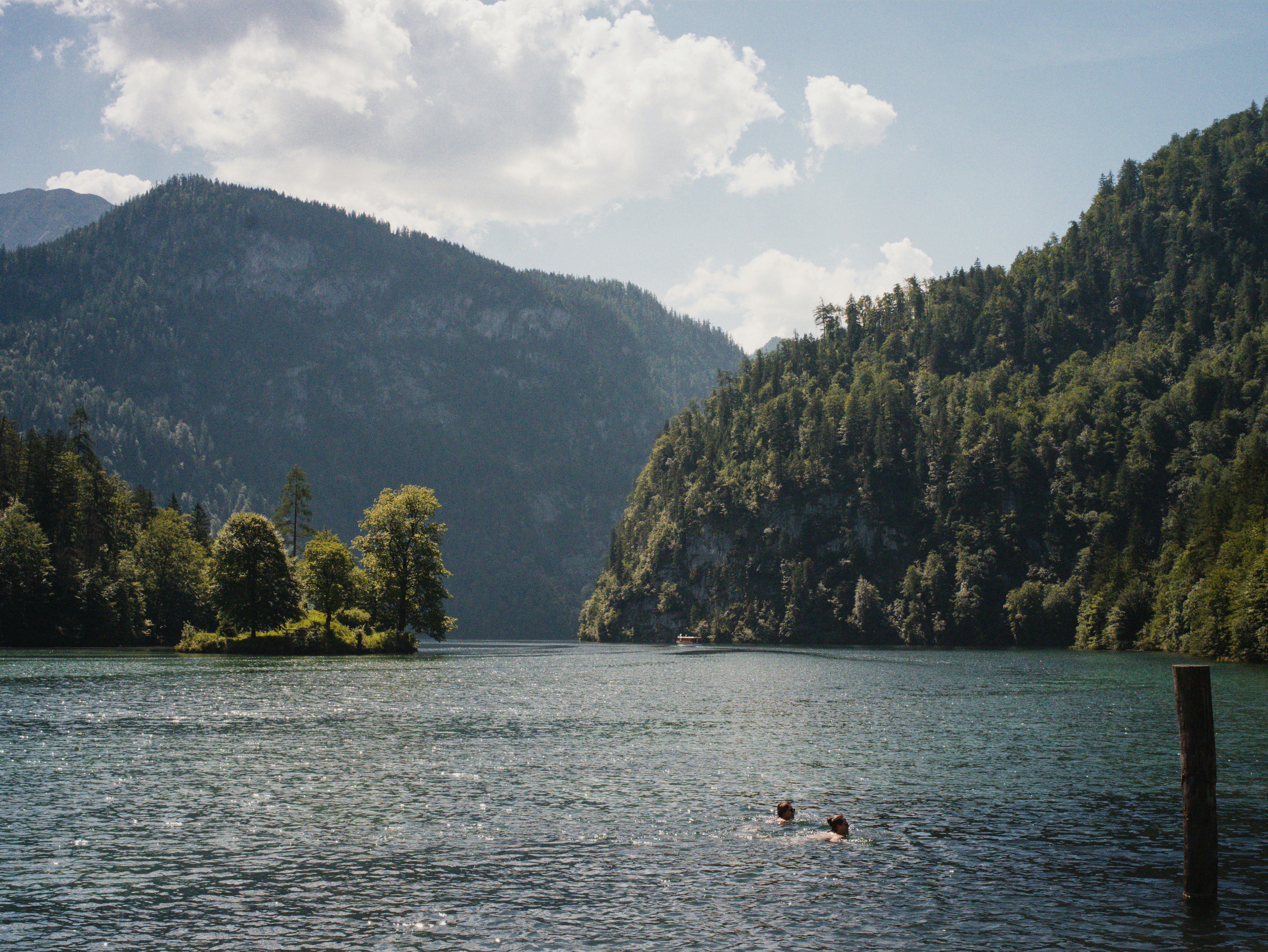 Two people swimming in a lake surrounded by steep forested mountains