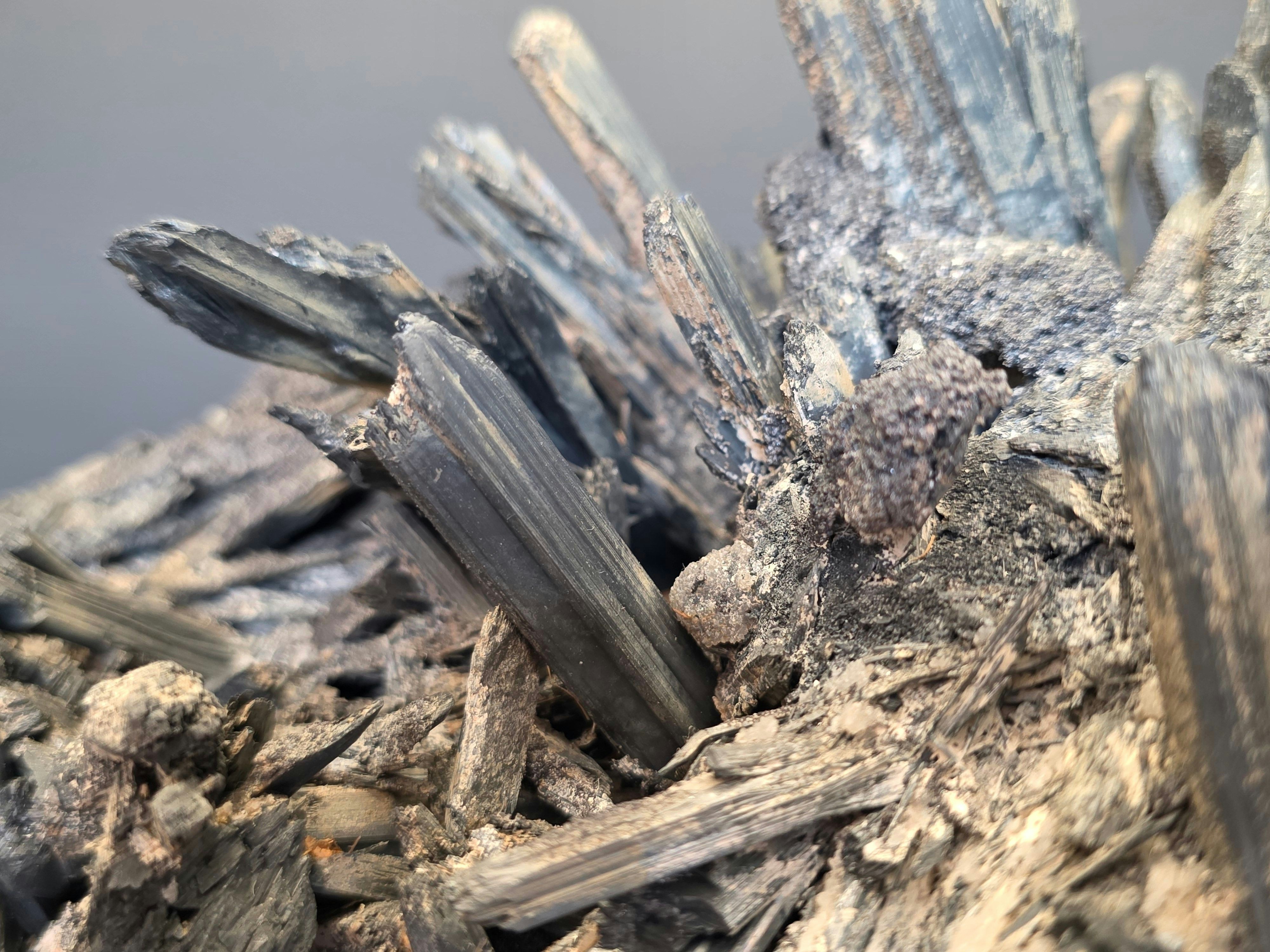 A cluster of dark grey needle-like mineral crystals on a rough textured base