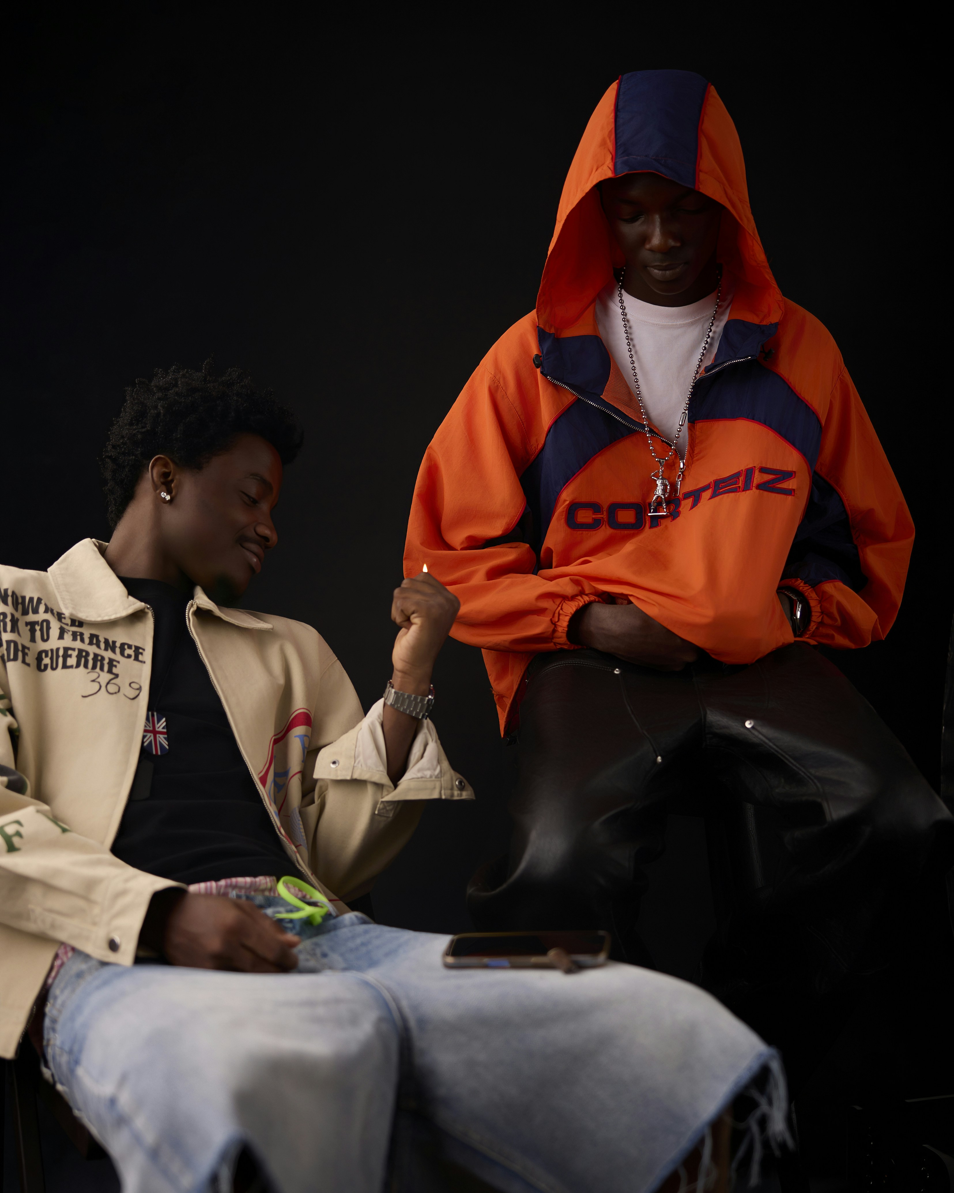 Two men in casual streetwear, one holding a lighter, against a black background