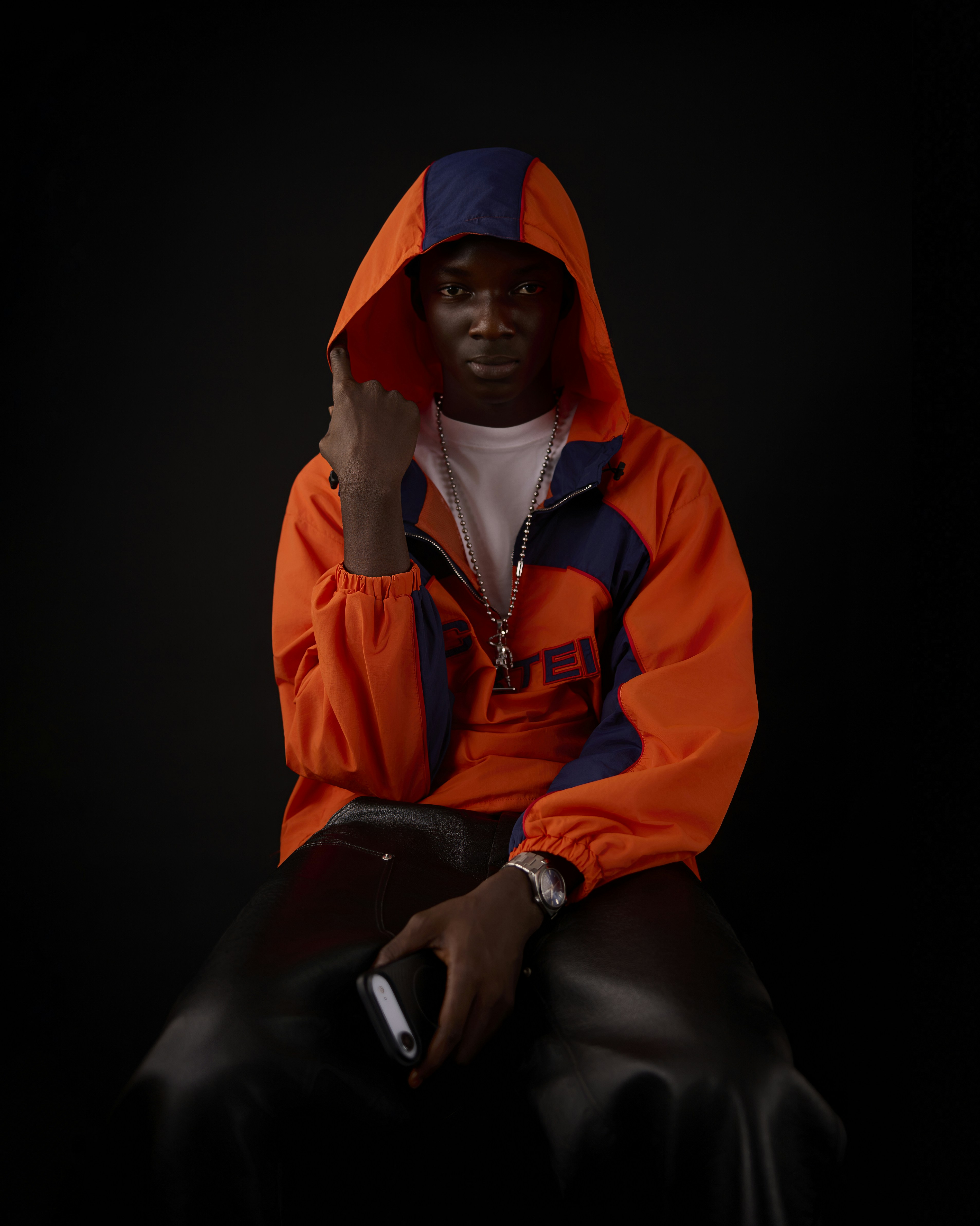 A man in an orange and blue hooded jacket holding a smartphone