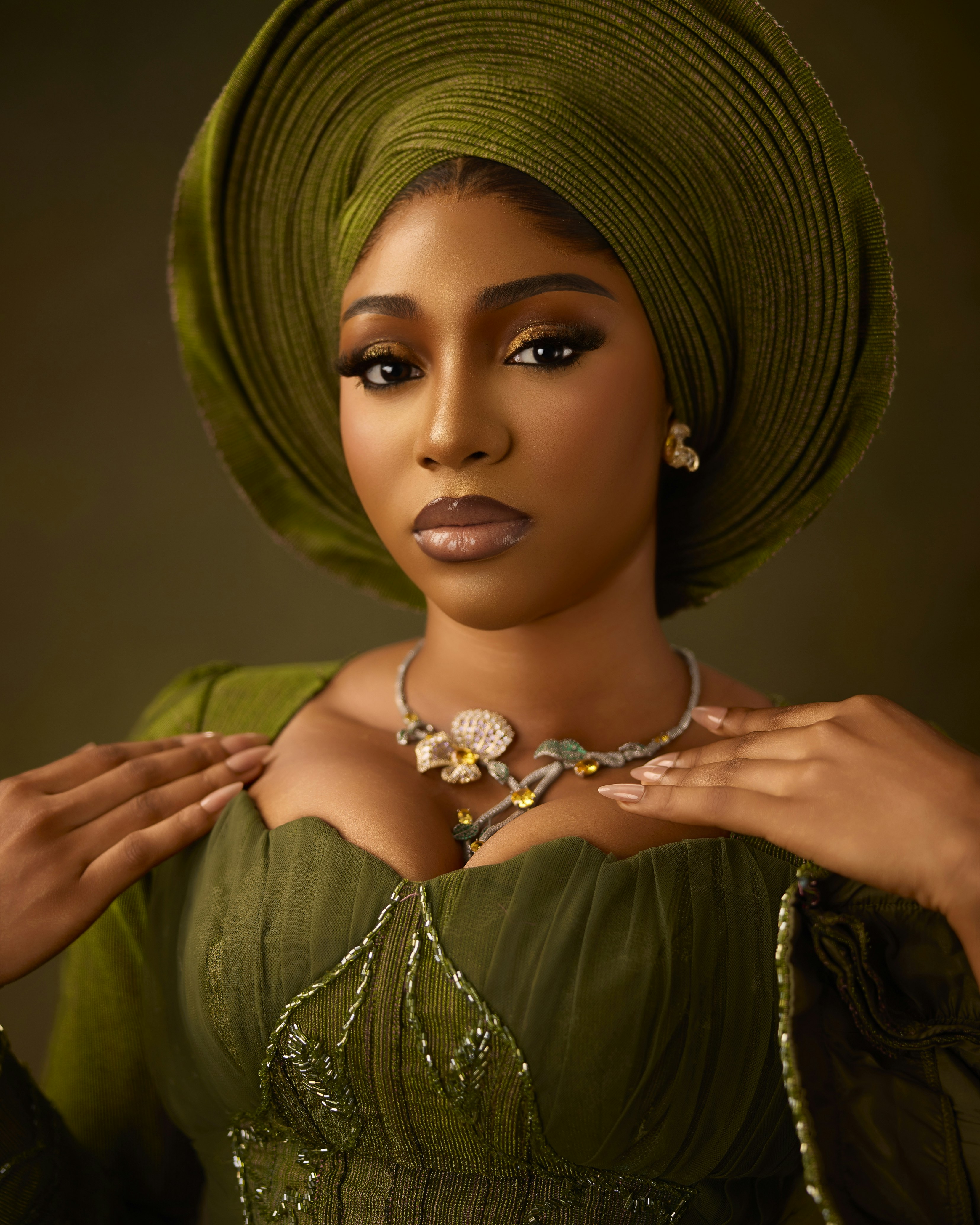 A woman wearing an olive green headwrap and matching dress with a floral necklace