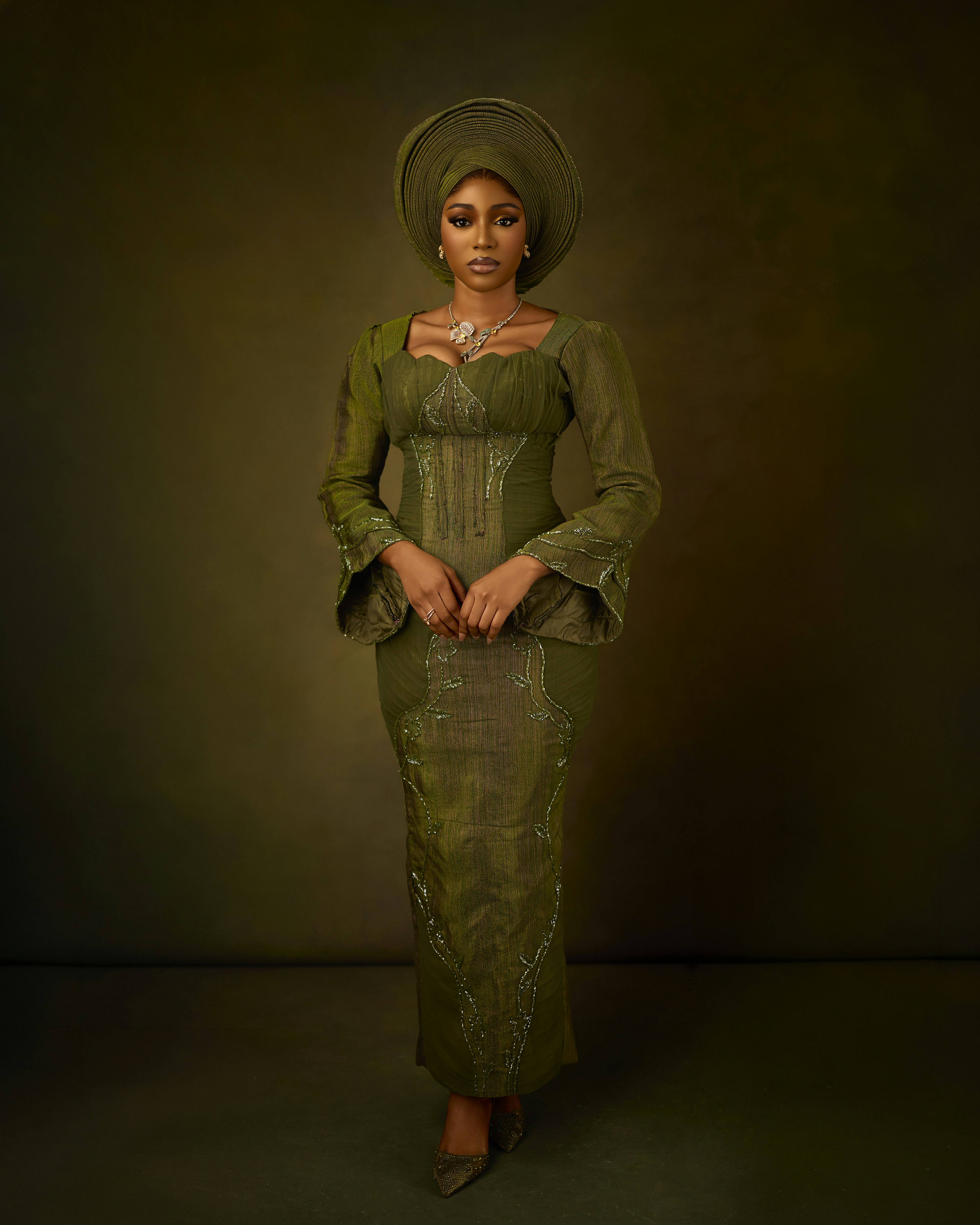 A woman in a green dress and matching headwrap against a dark background
