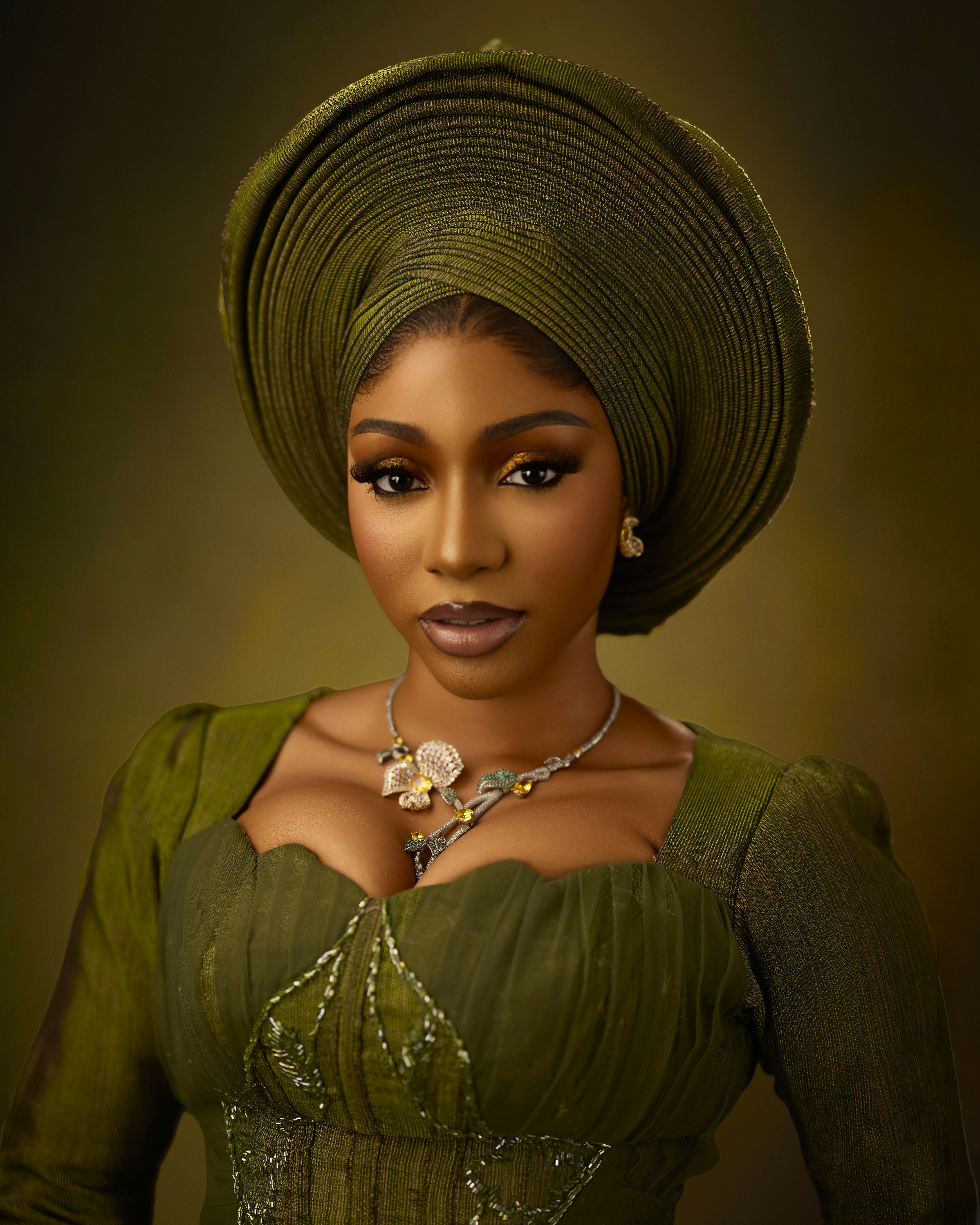 A woman wearing a green headwrap and matching dress with a floral necklace