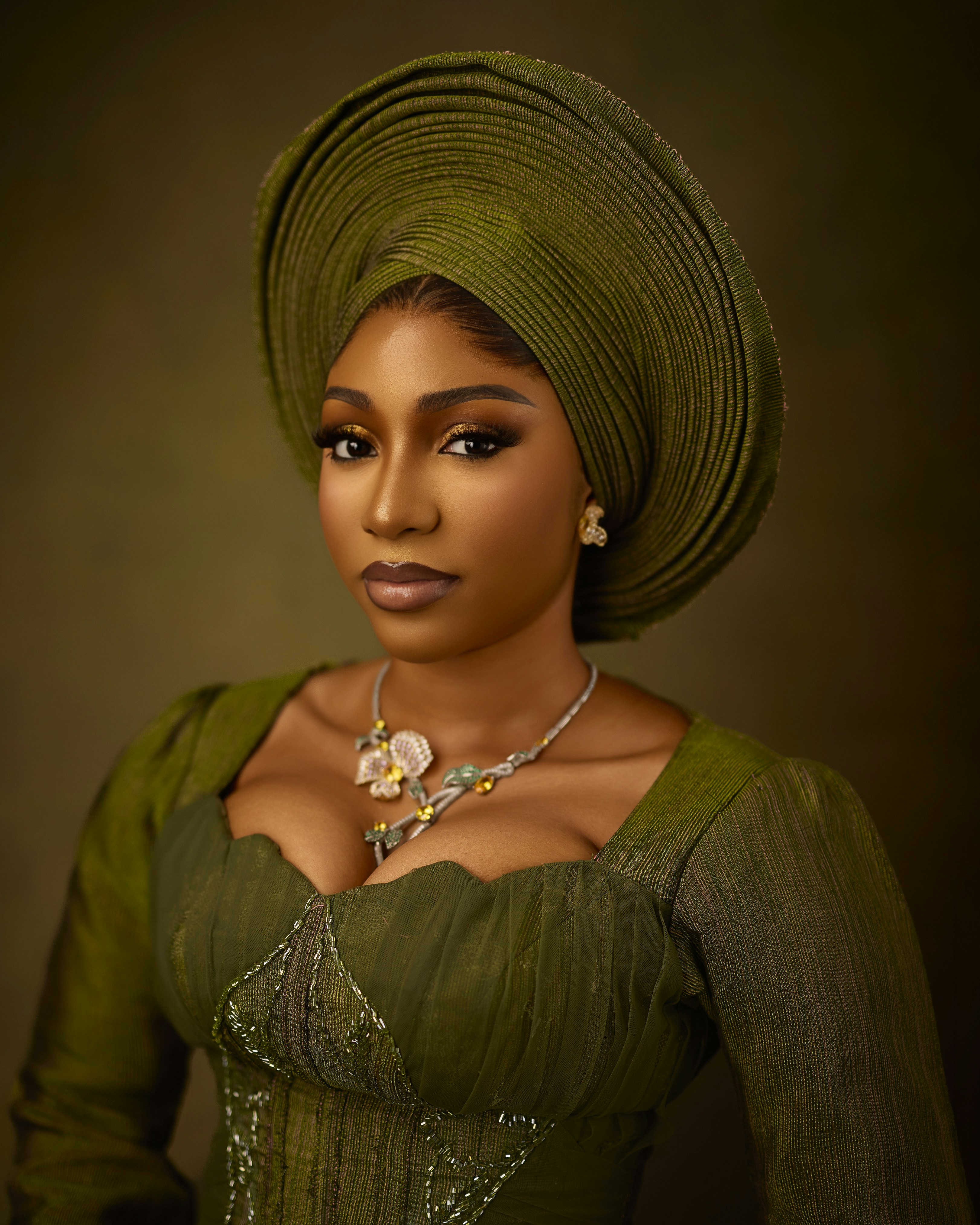 A woman wearing a green gele headwrap and matching dress with a floral necklace