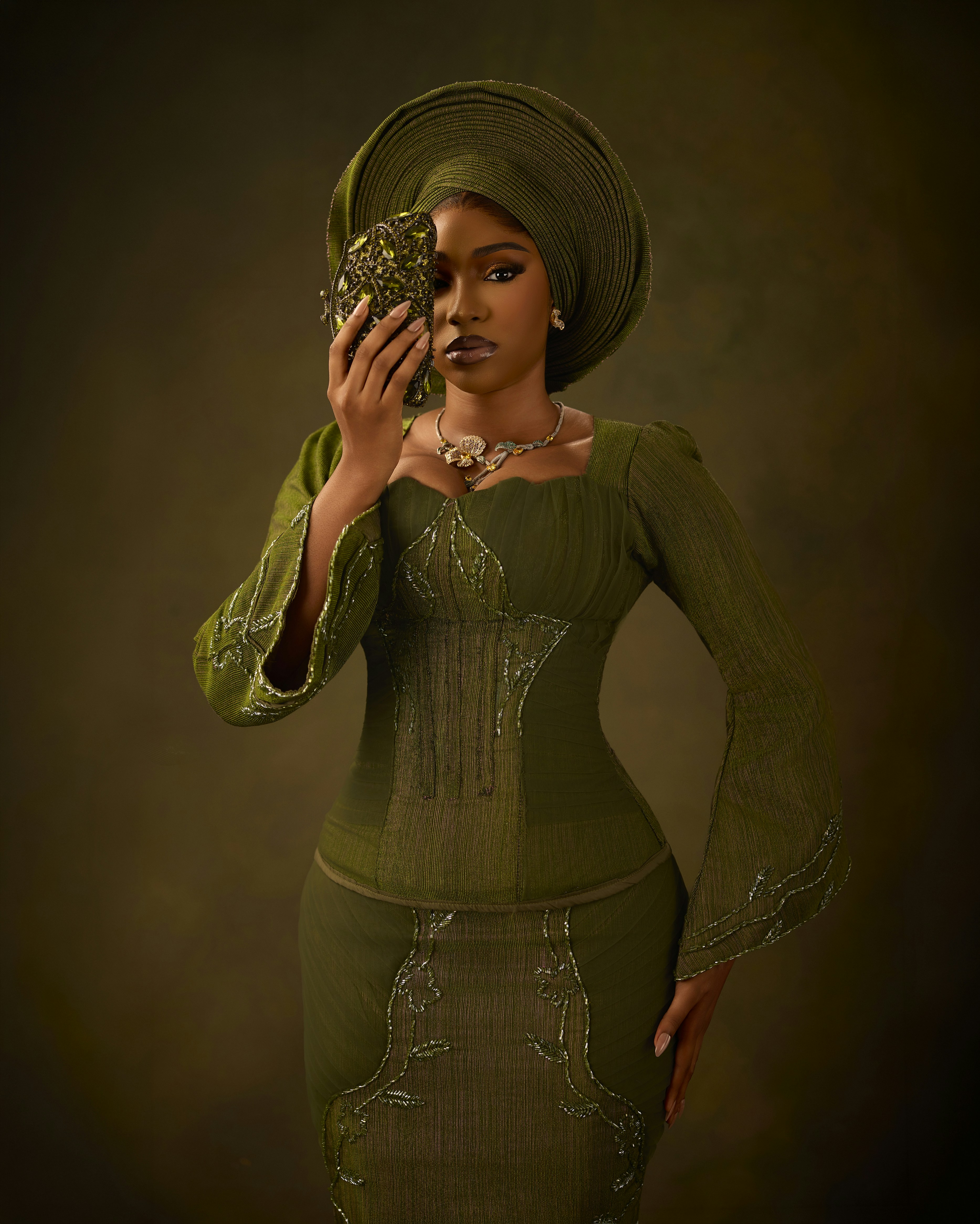 A woman in a green traditional outfit and headwrap holding a beaded clutch