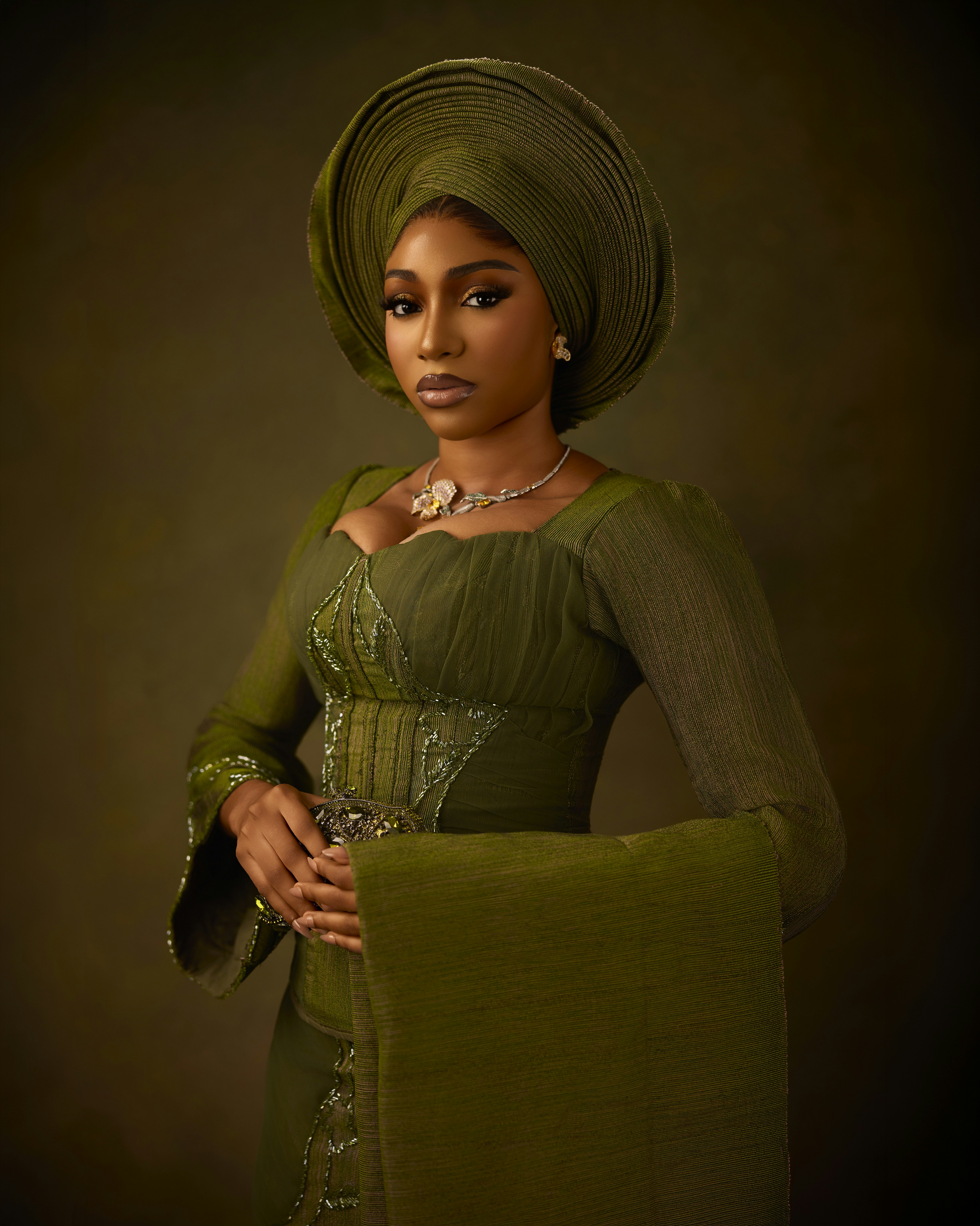 A woman in a green dress and matching headwrap against a dark background