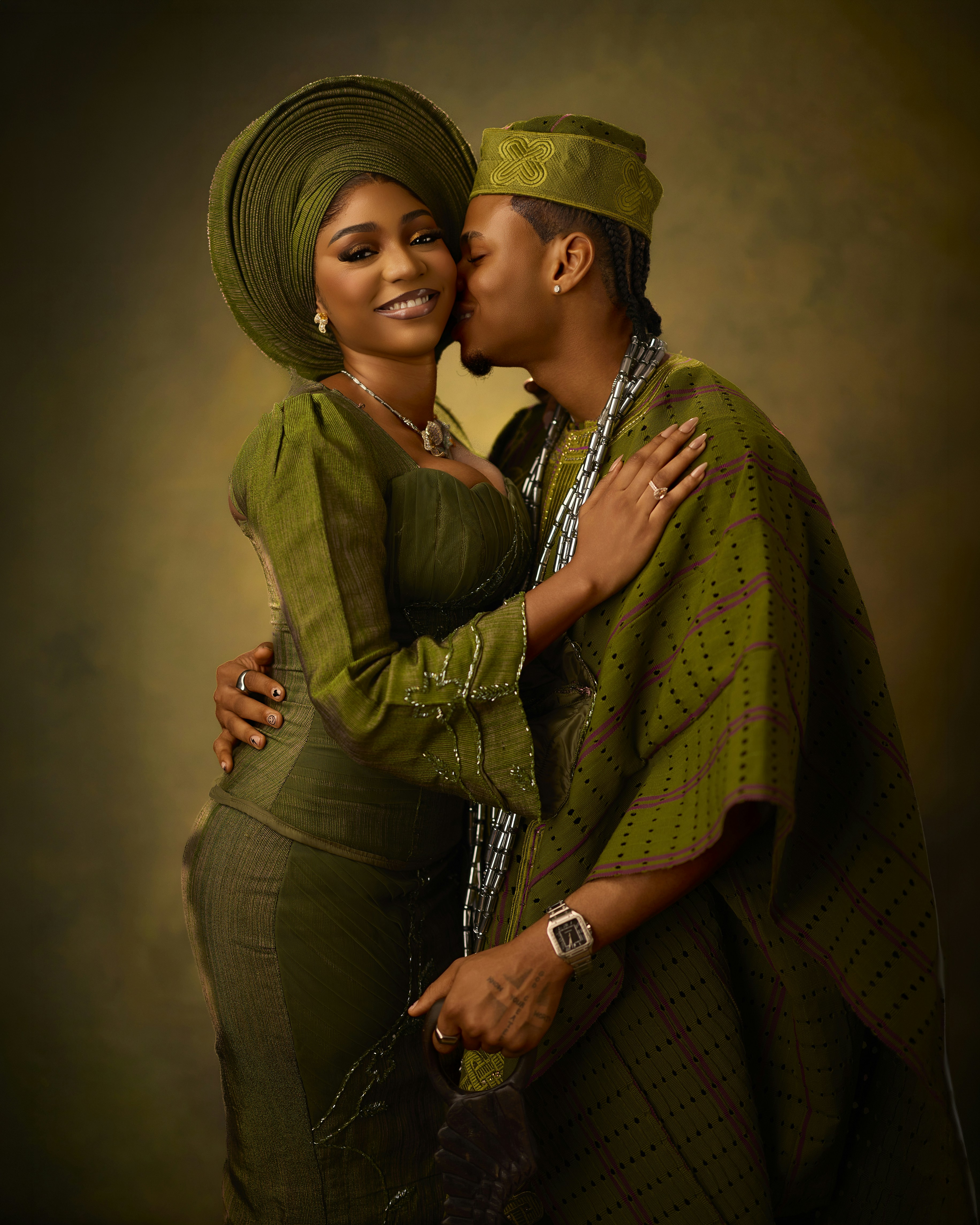 A man kissing a woman on the cheek, both wearing traditional olive green attire