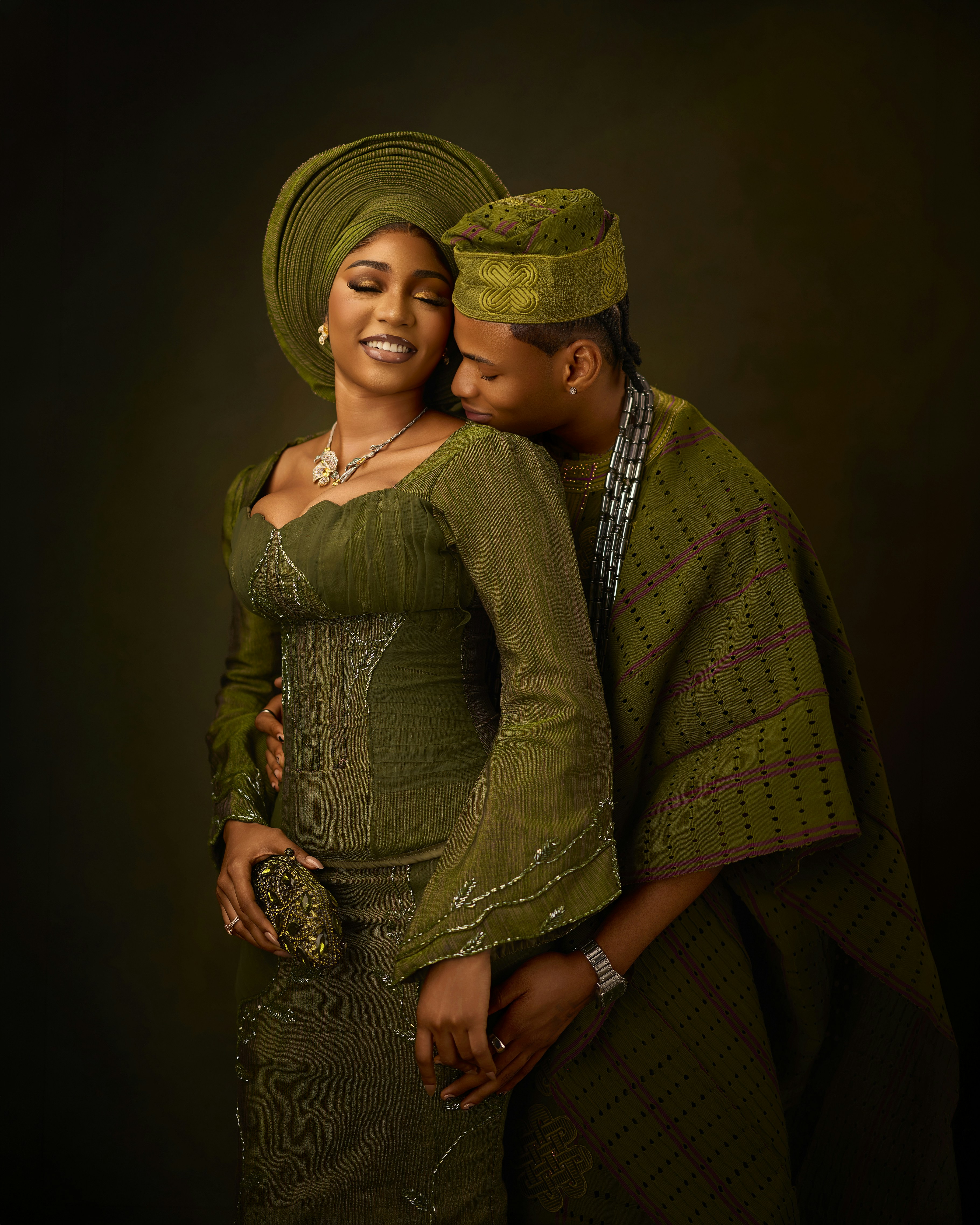 A woman in a green traditional outfit and headwrap embraced by a man