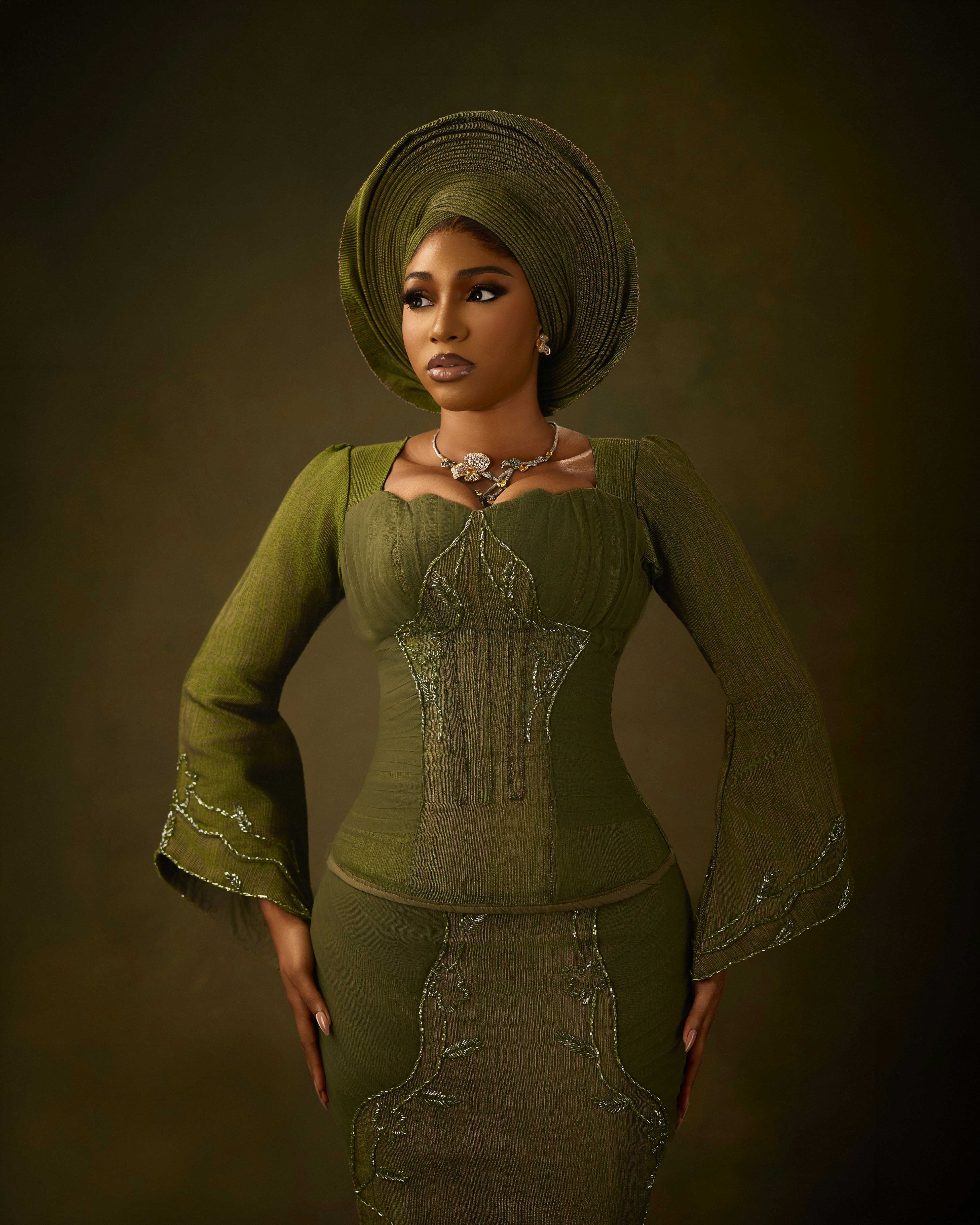 A woman in a green dress and matching headwrap against a dark background