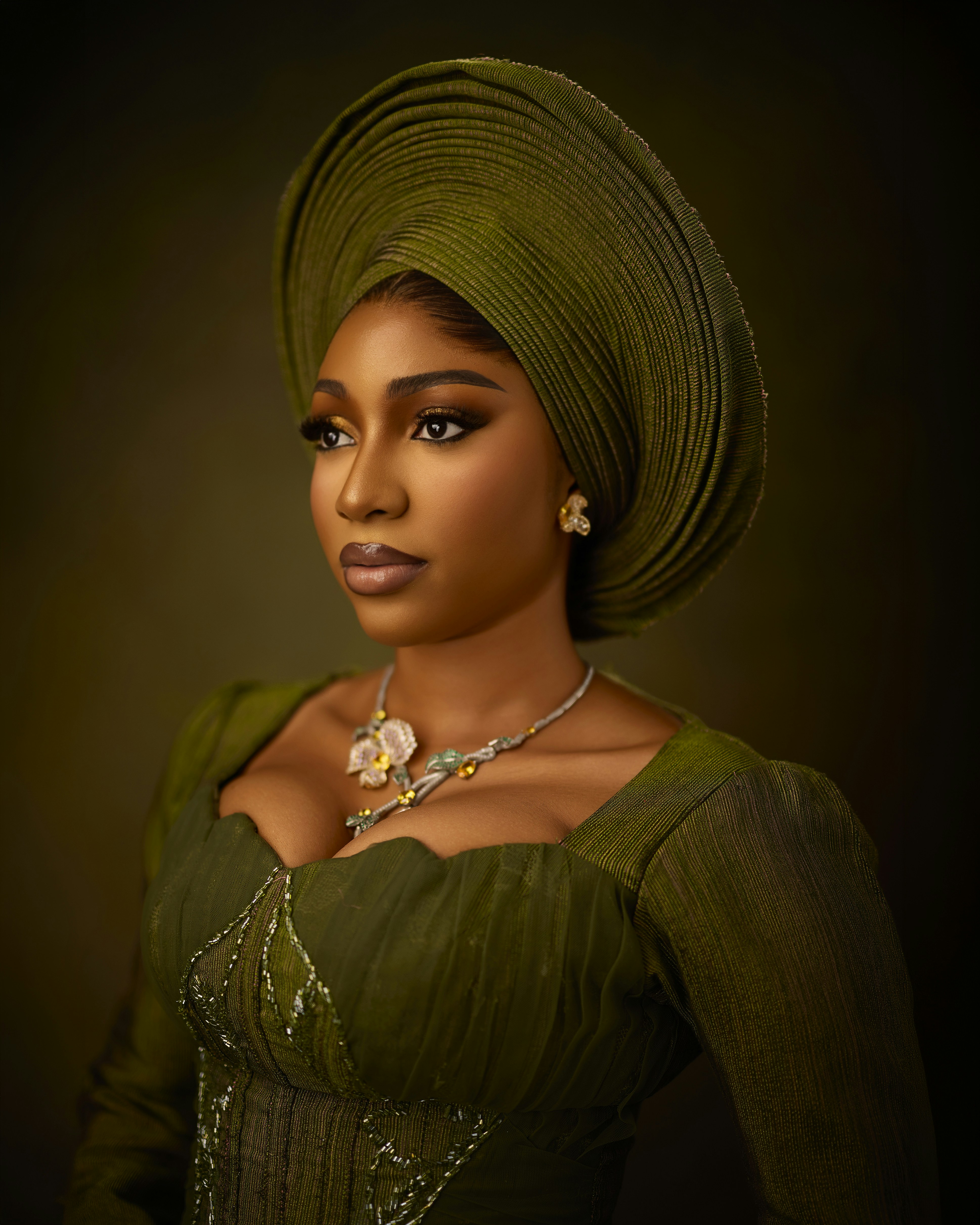 A woman wearing a green gele headwrap and matching dress with a floral necklace