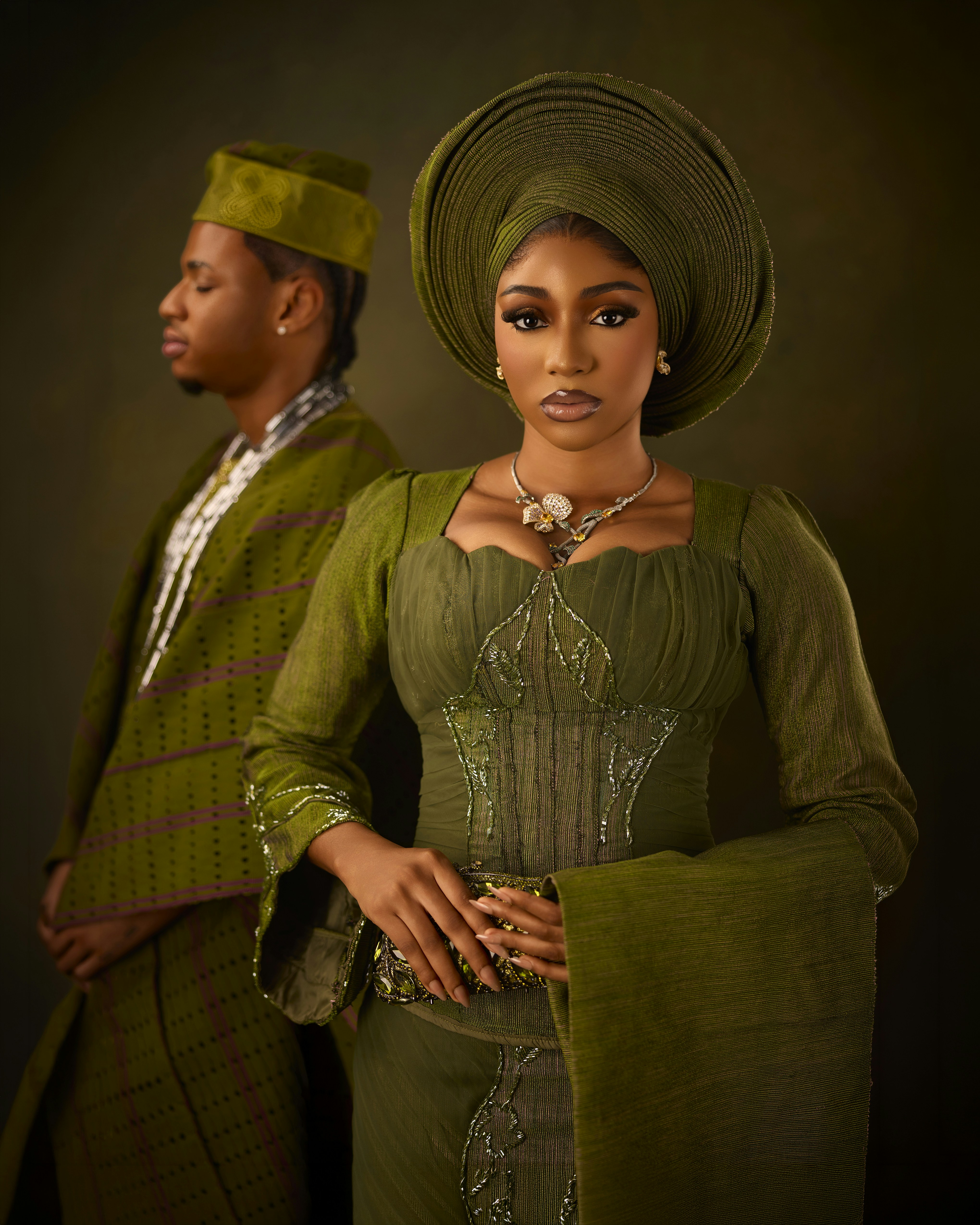 A woman and a man in traditional olive green attire against a dark background