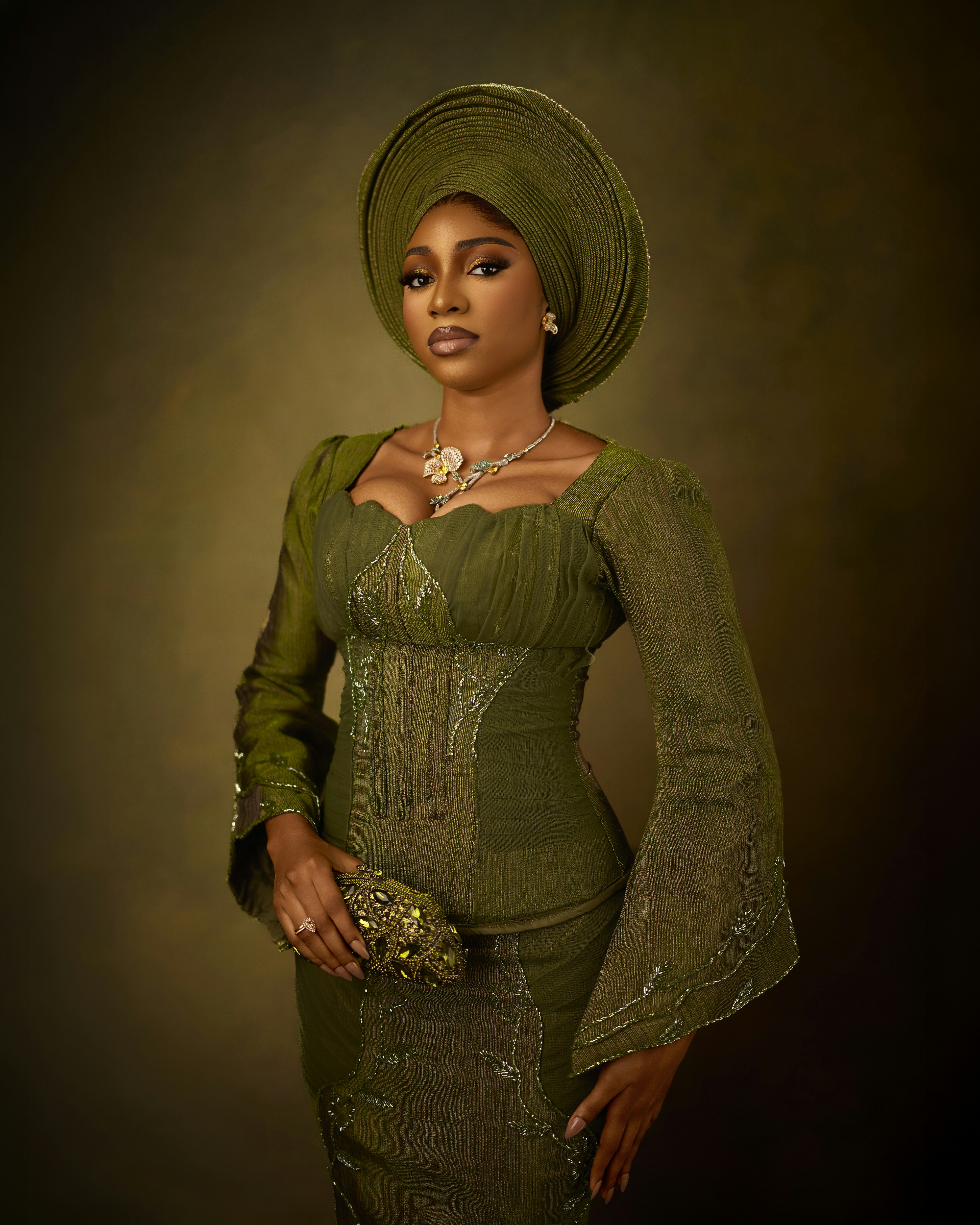 A woman in a green traditional dress and headwrap holding a small embellished clutch
