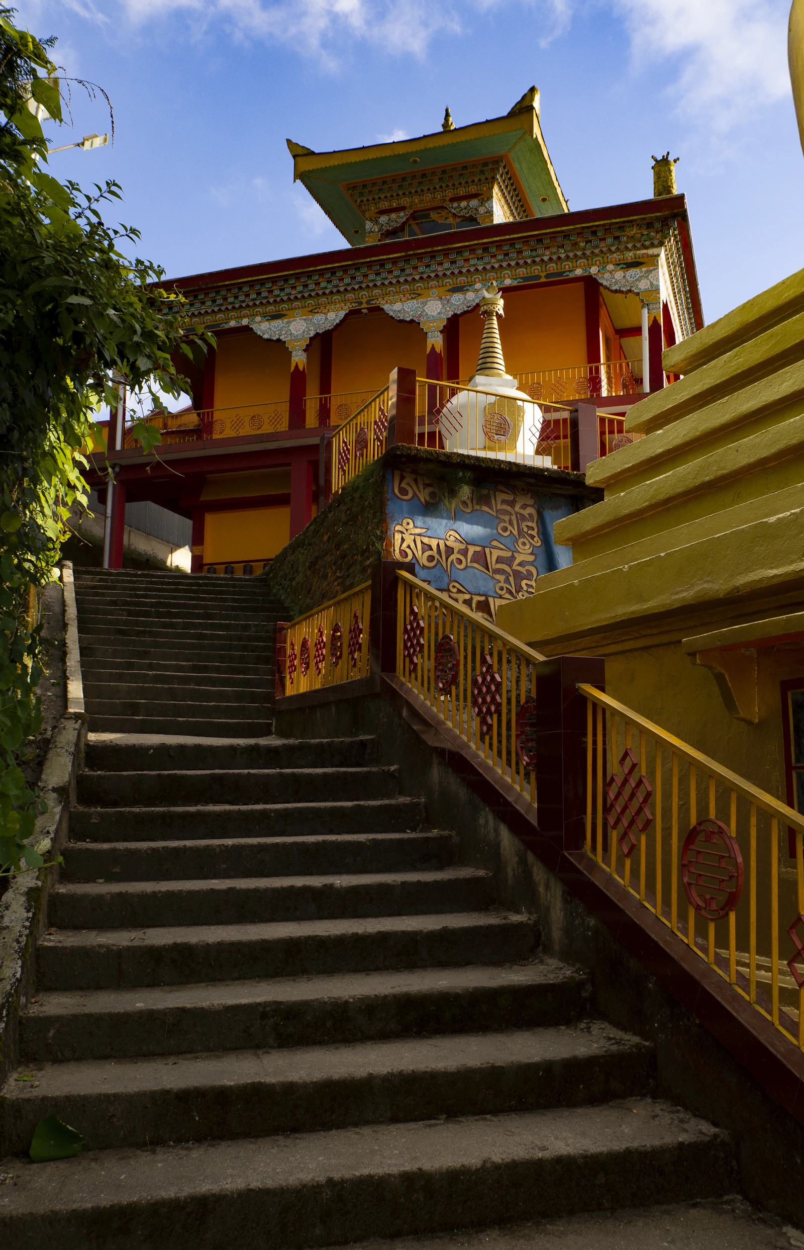 Stone steps rising to a painted Buddhist monastery in Darjeeling, with a white stupa and carved mantra