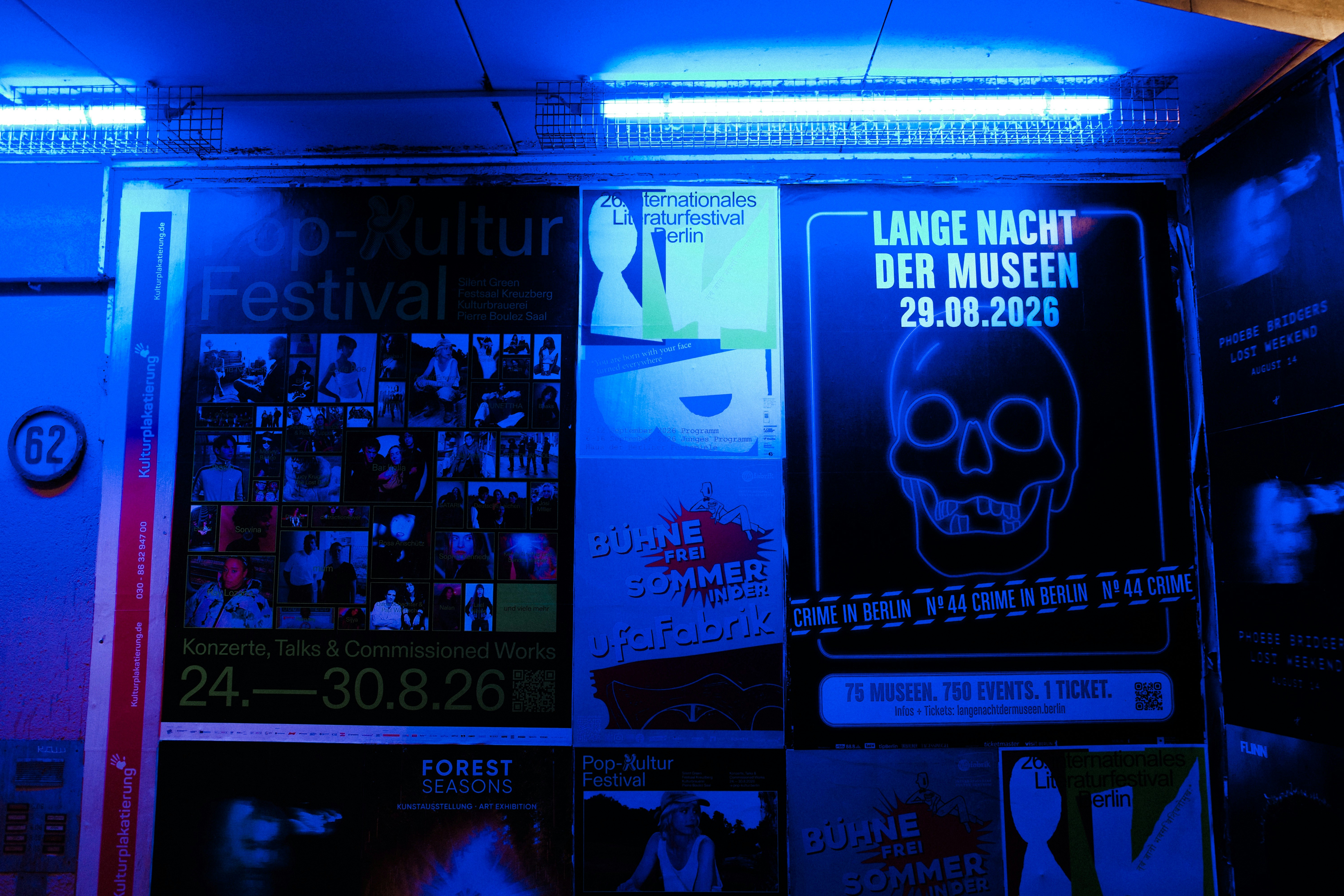 Posters for cultural events on a wall illuminated by bright blue neon lights