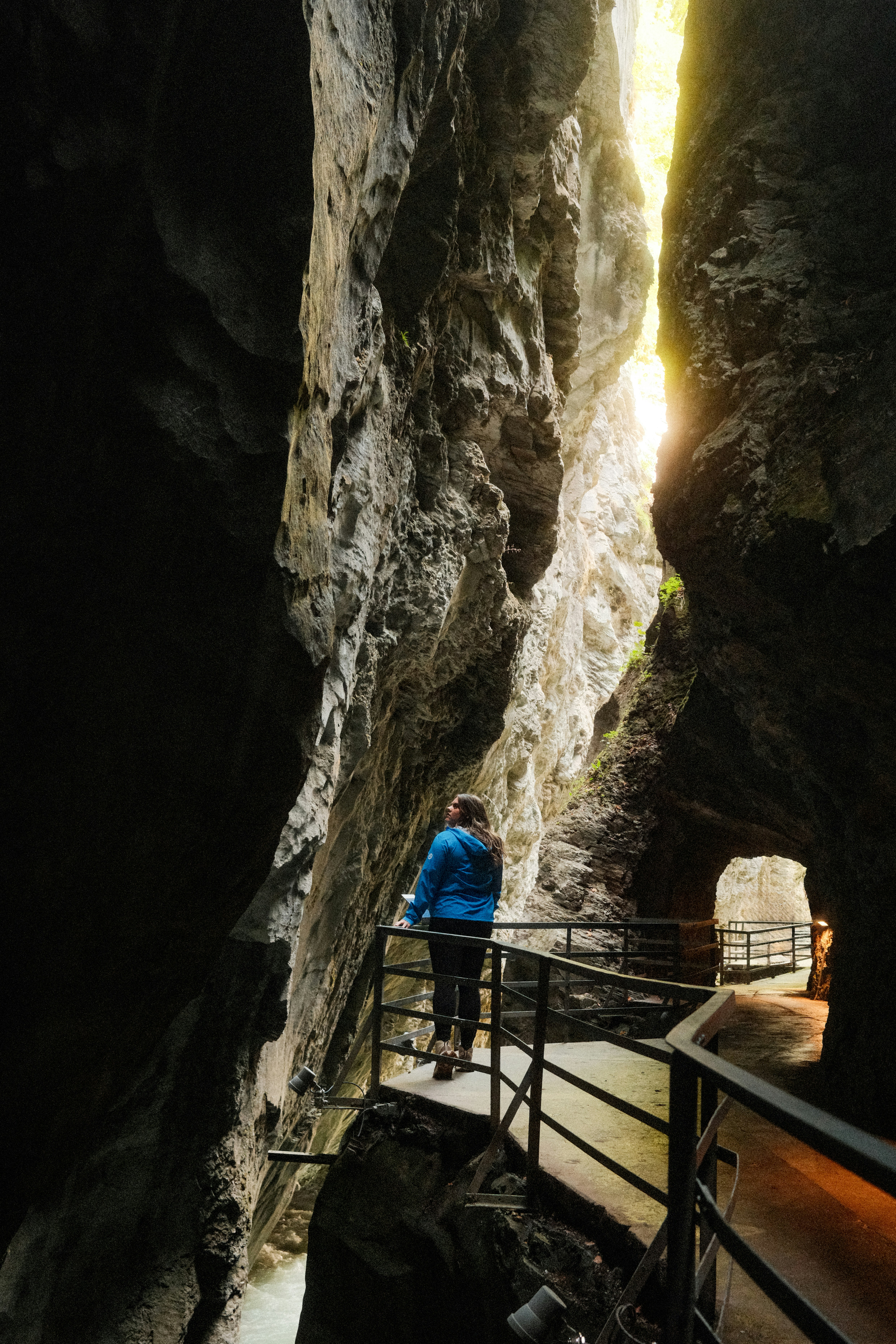 A person in a blue jacket on a metal walkway inside a narrow gorge