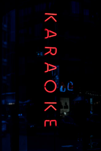 A vertical red neon sign reading "KARAOKE" against a dark night background