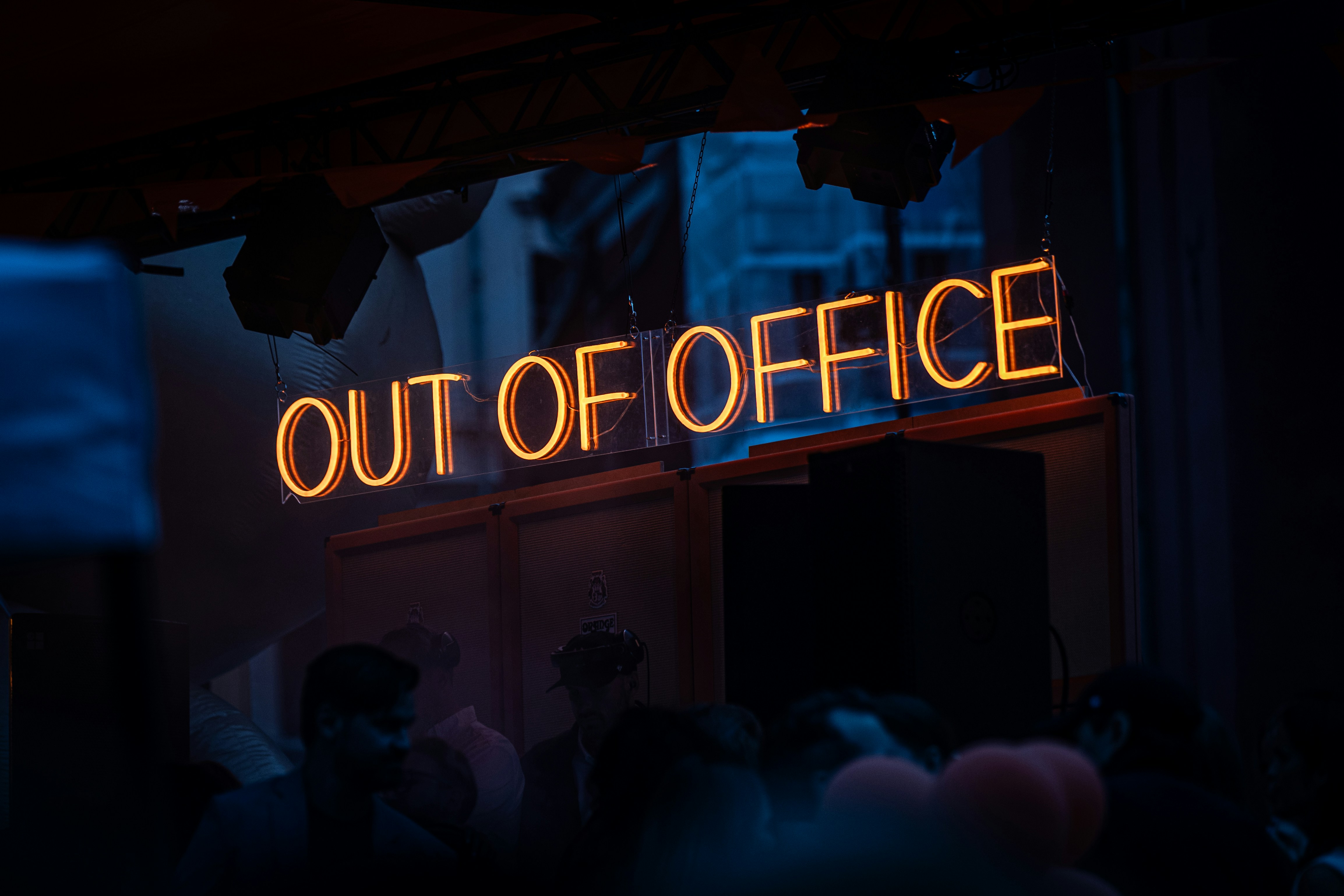 A glowing orange neon sign reading "OUT OF OFFICE" above a dark room