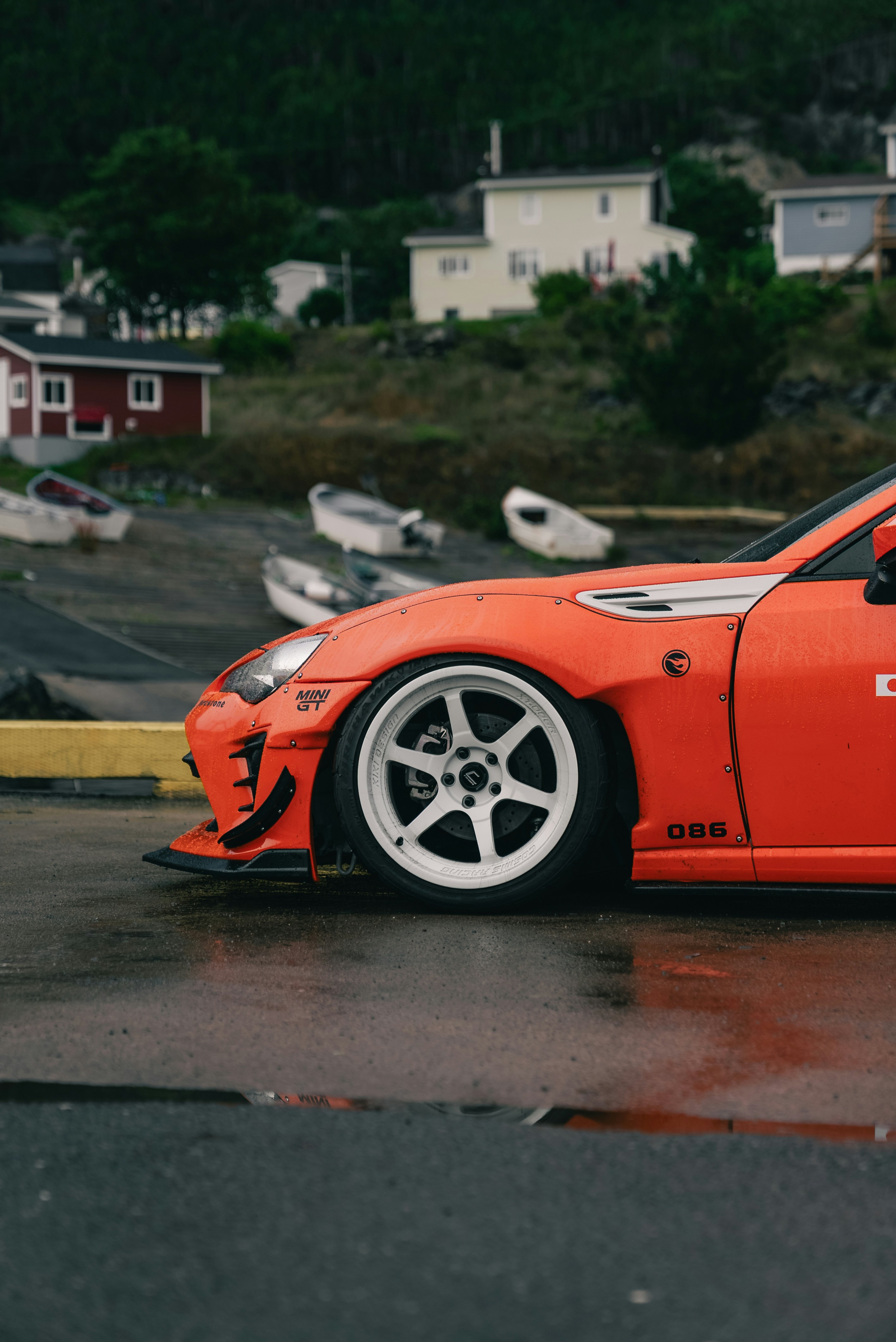 An orange sports car with white wheels parked on a wet harbor pier