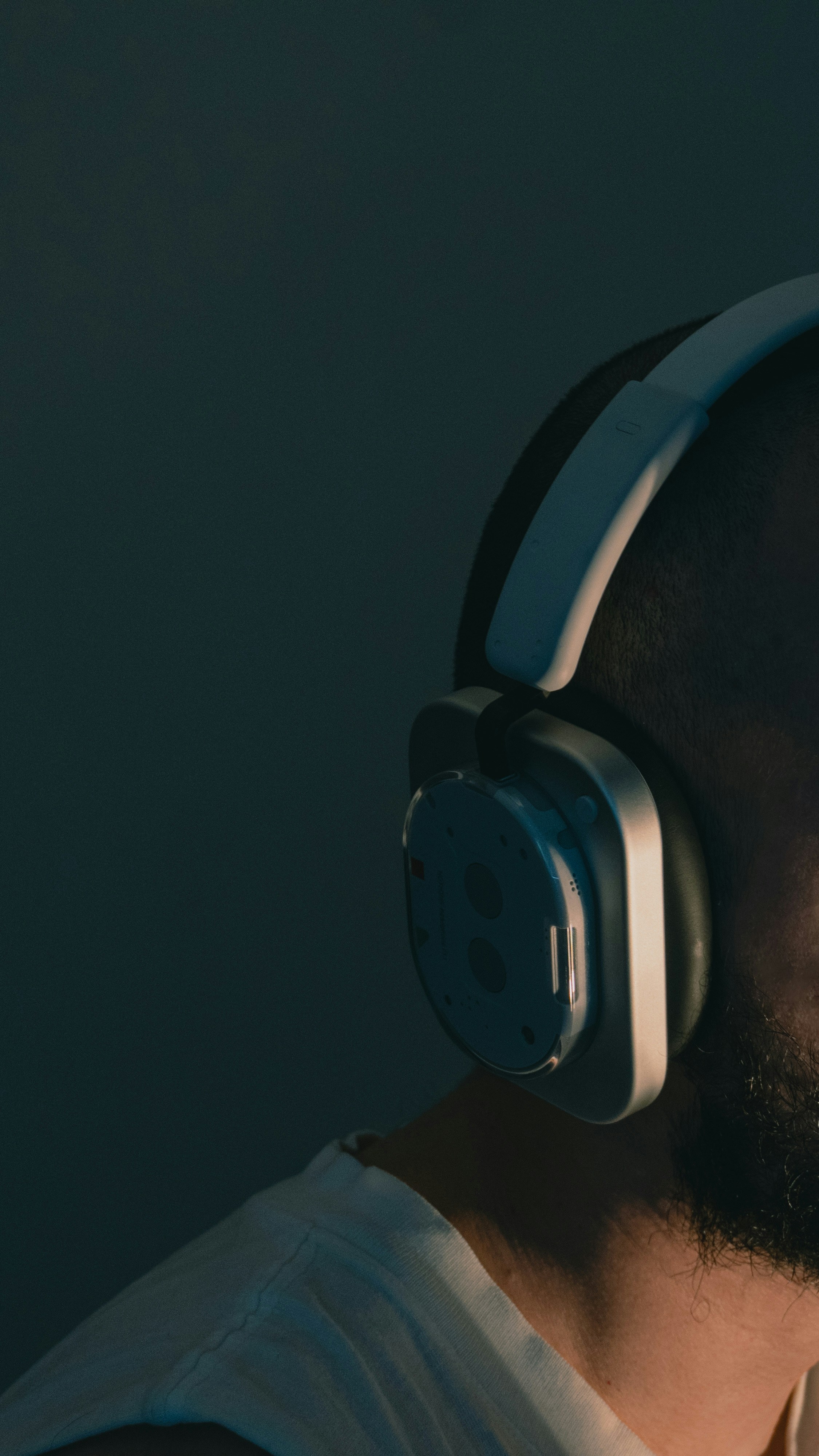 A person wearing white over-ear headphones in a dimly lit room