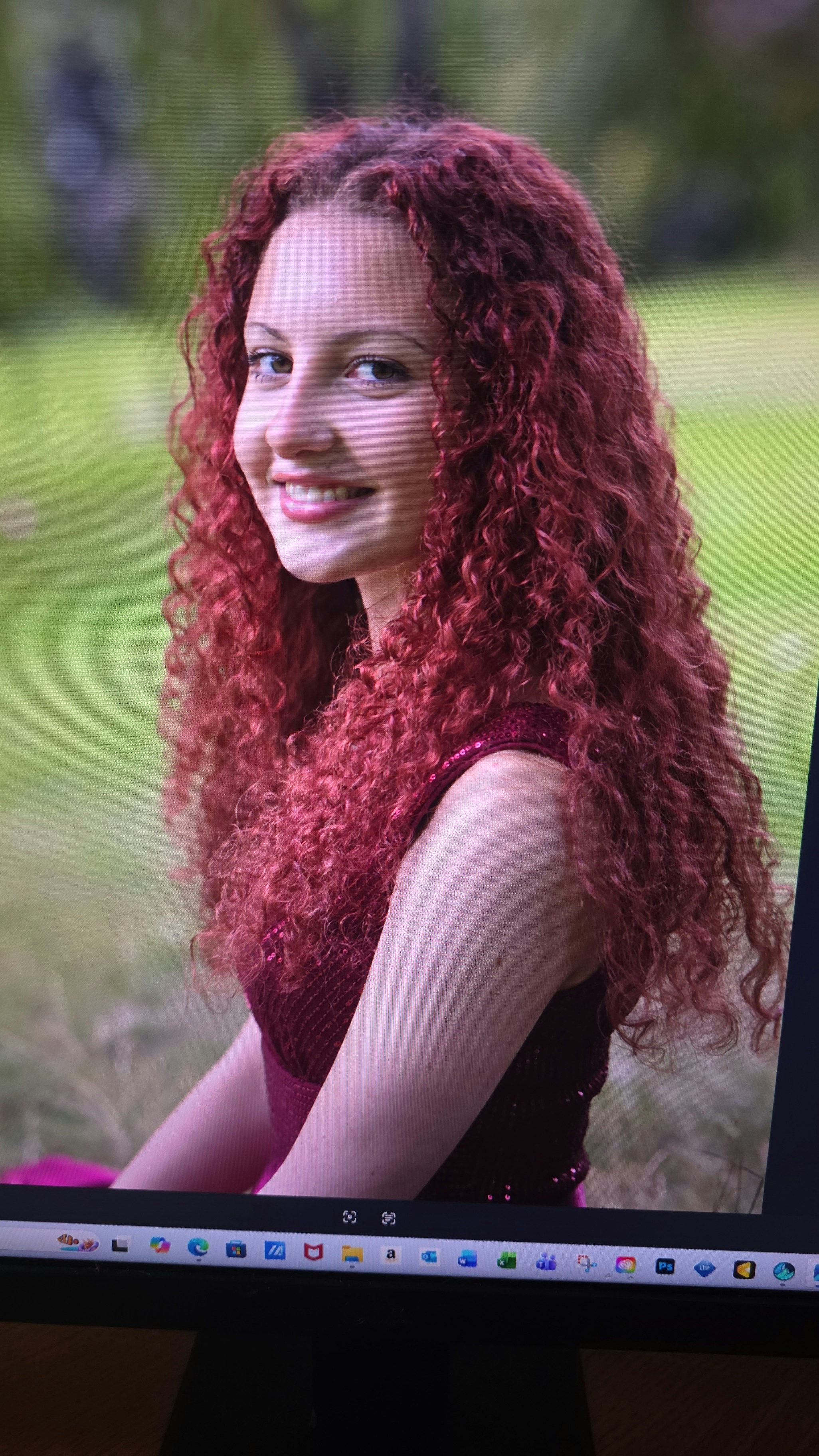 A smiling young woman with long curly red hair in a maroon dress