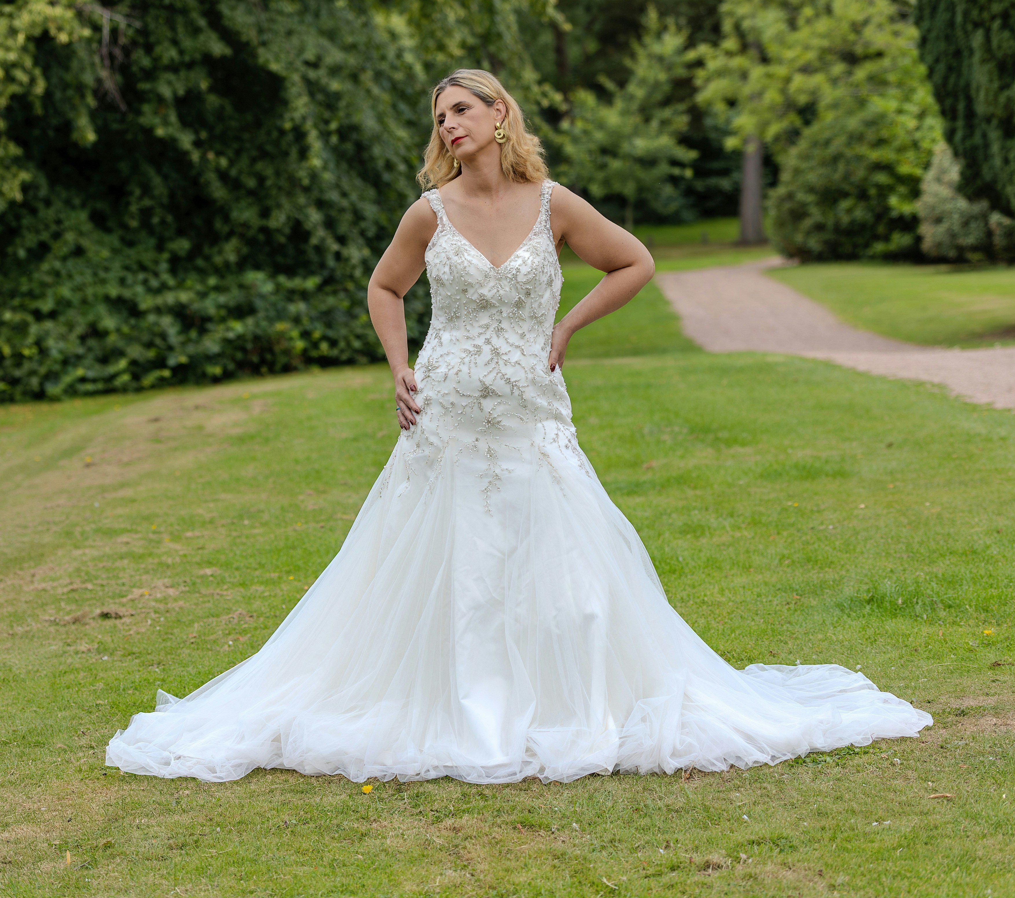 A woman in a white beaded wedding dress posing on a green lawn