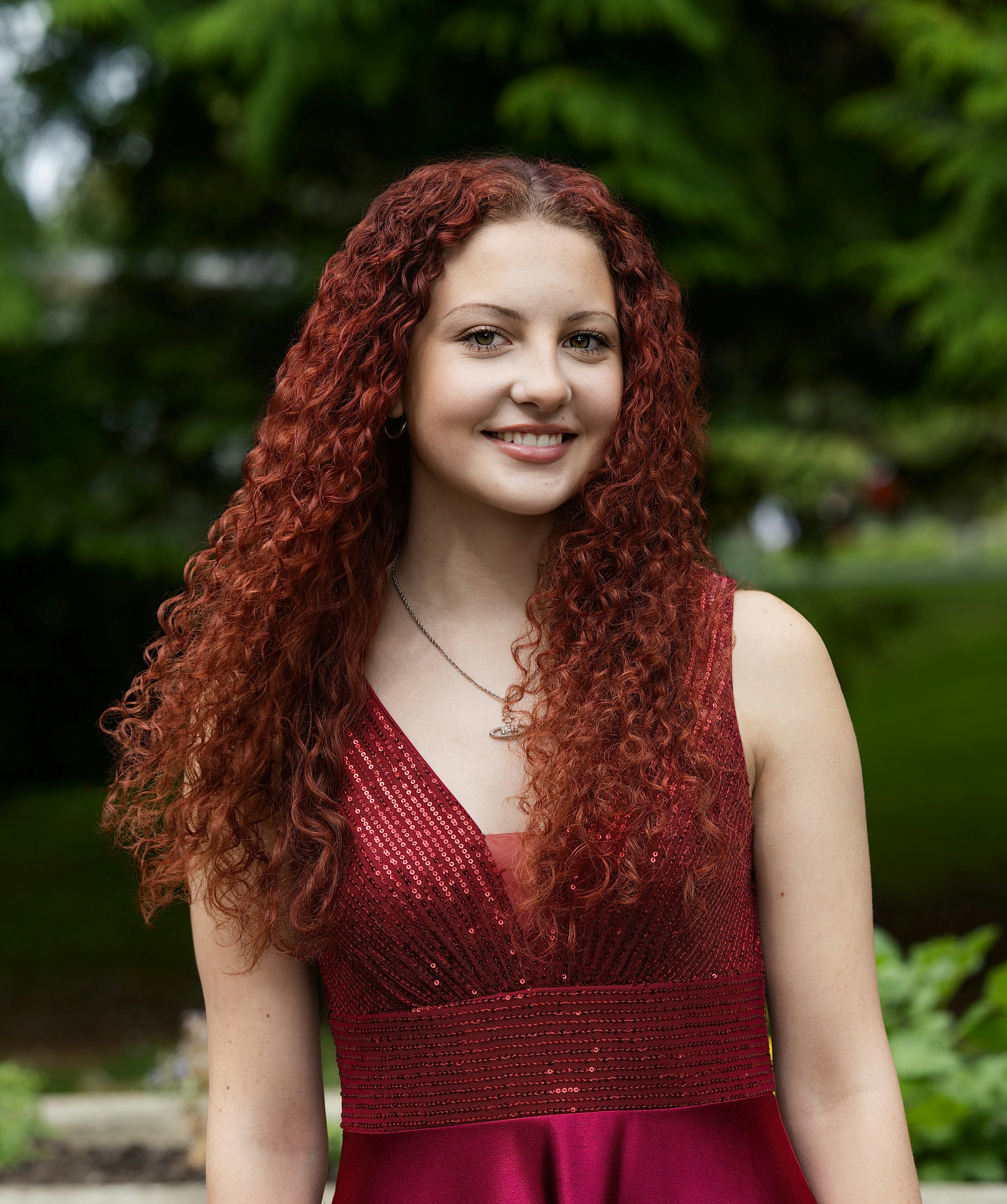 A young woman with long curly red hair wearing a sequined maroon dress