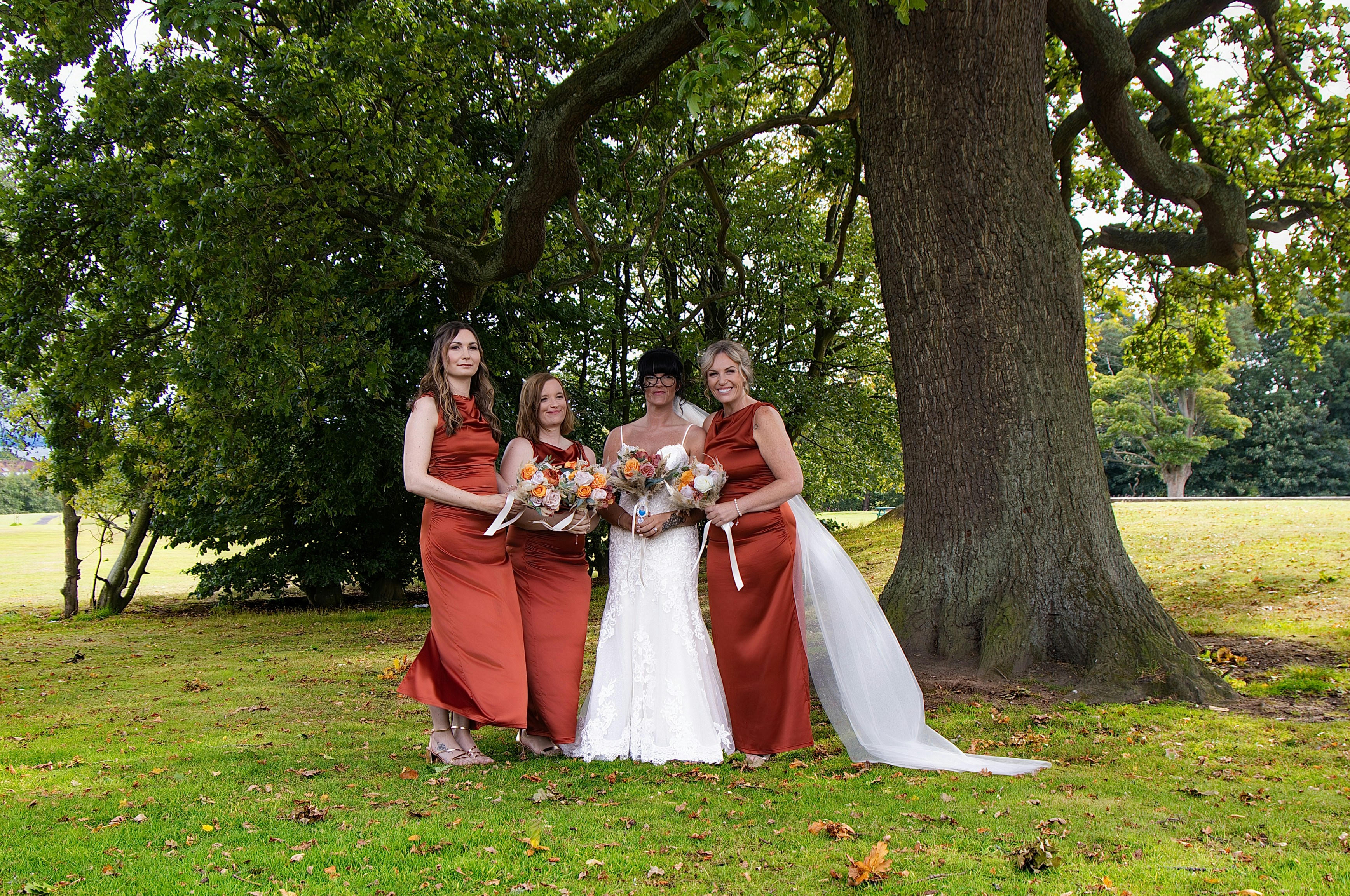 A bride in a white dress and three bridesmaids in rust-colored dresses outdoors