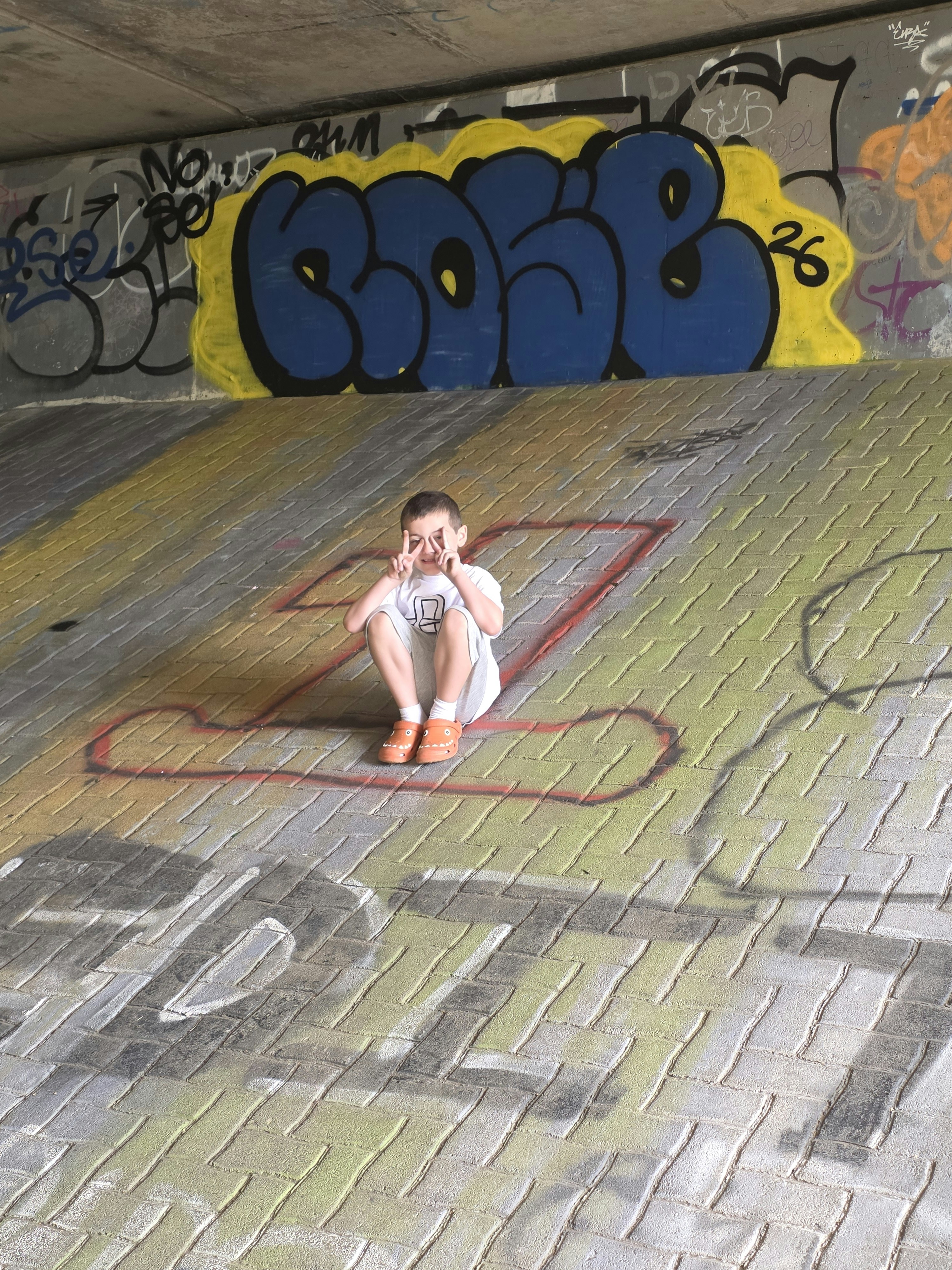A child in a white t-shirt making a peace sign on a graffiti-covered slope