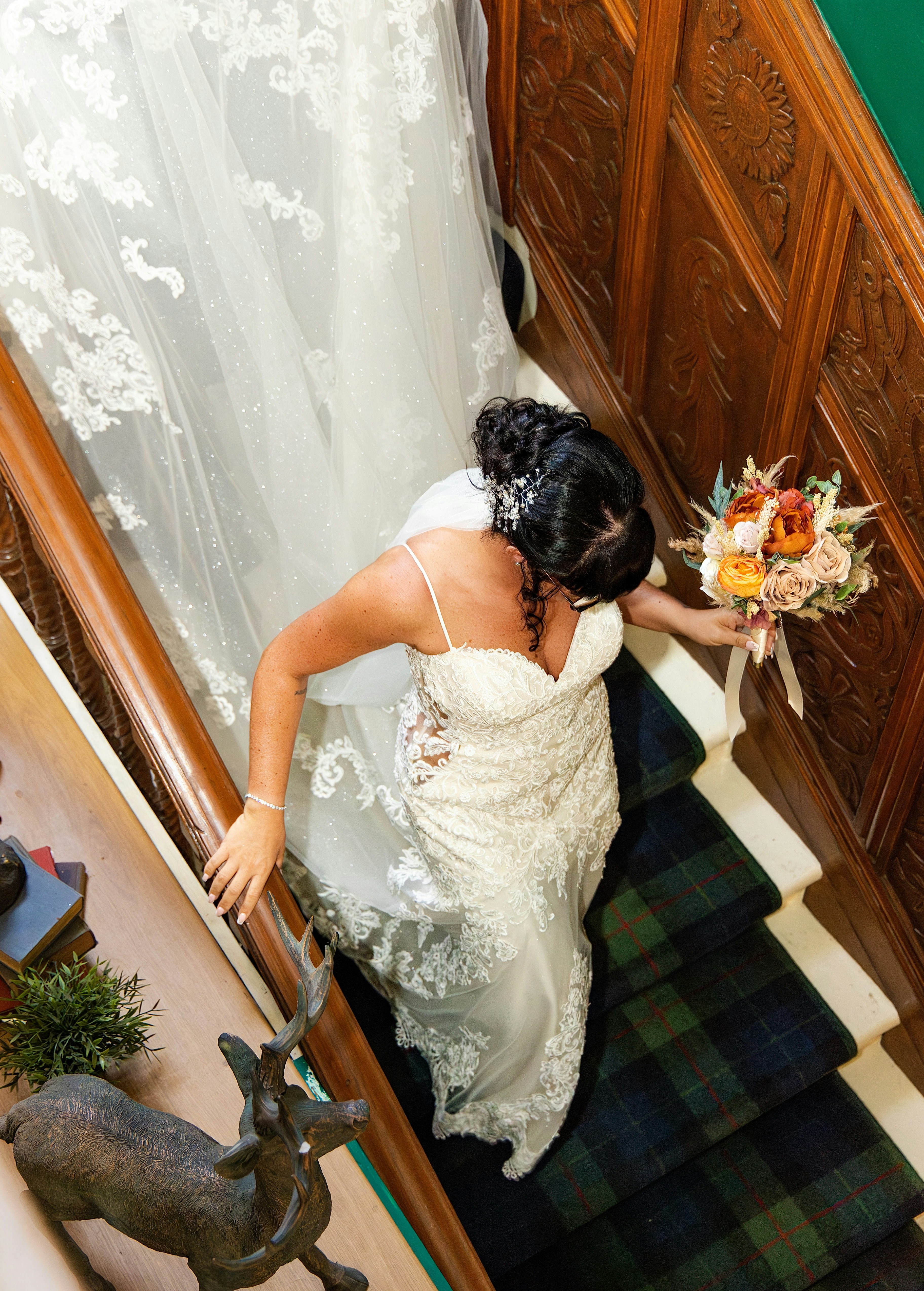 A bride in a lace wedding dress walking down a staircase with a bouquet