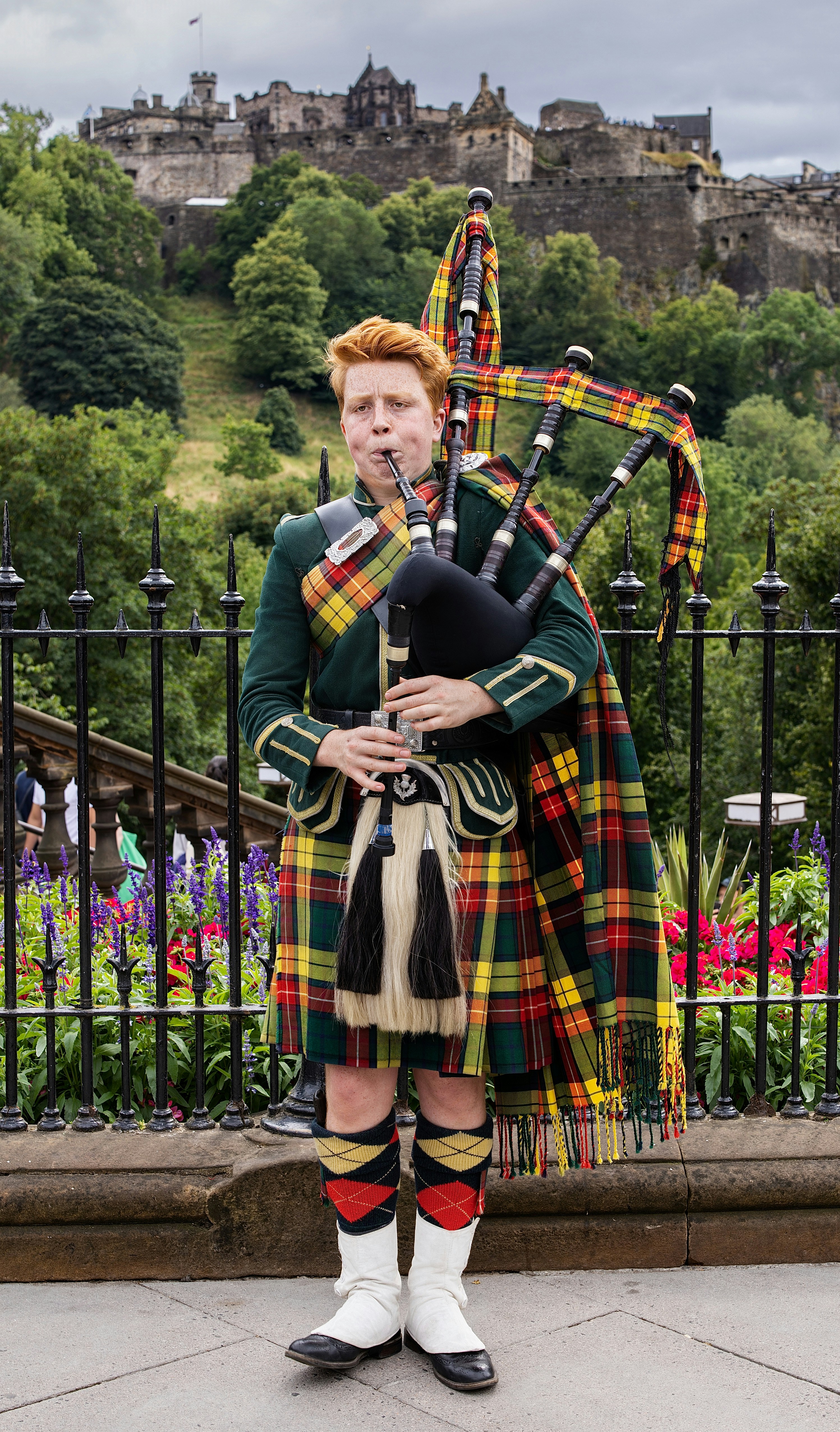 A person in traditional Scottish attire playing bagpipes before Edinburgh Castle in Scotland