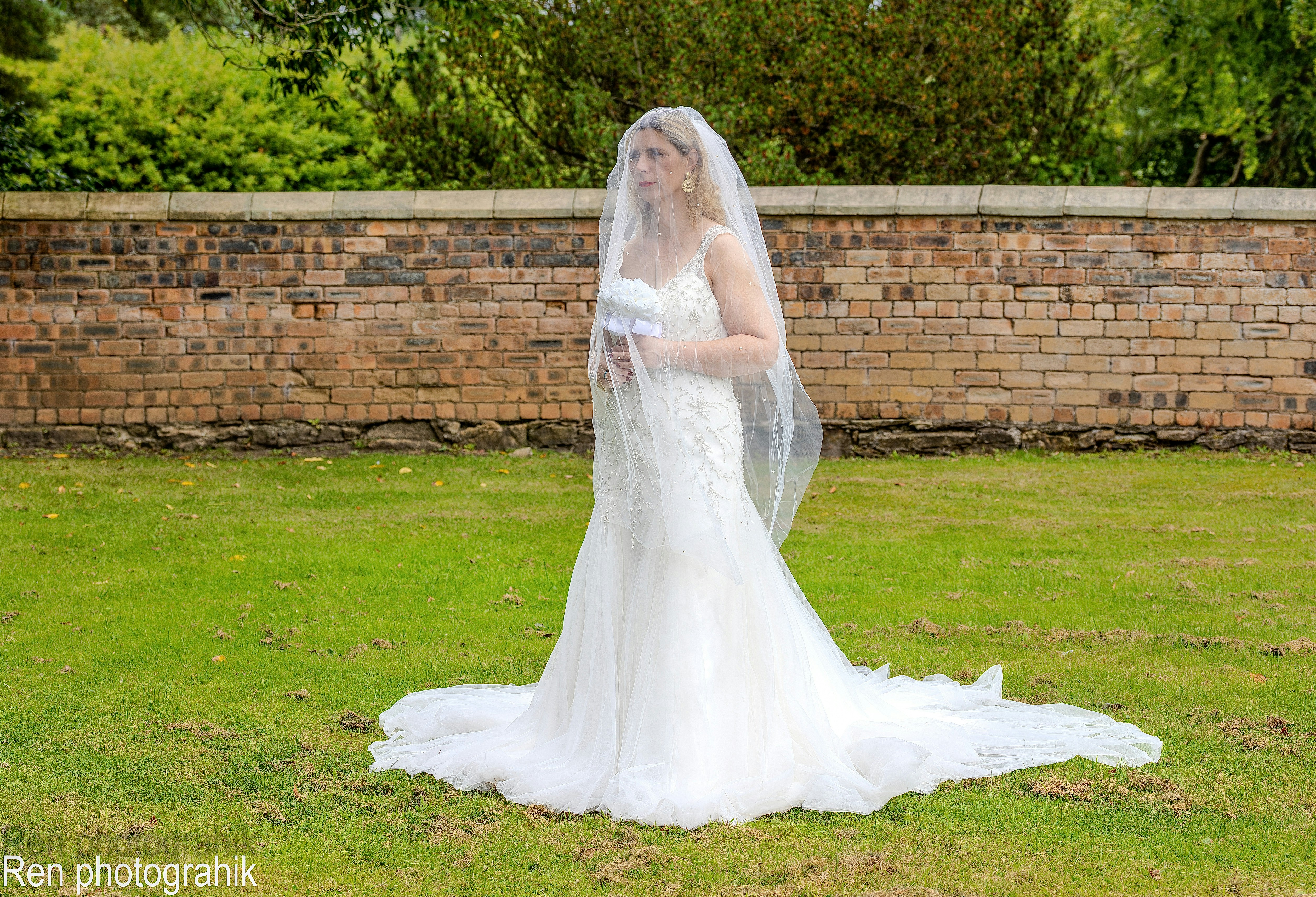 A woman in a white wedding dress and veil holding a bouquet on grass
