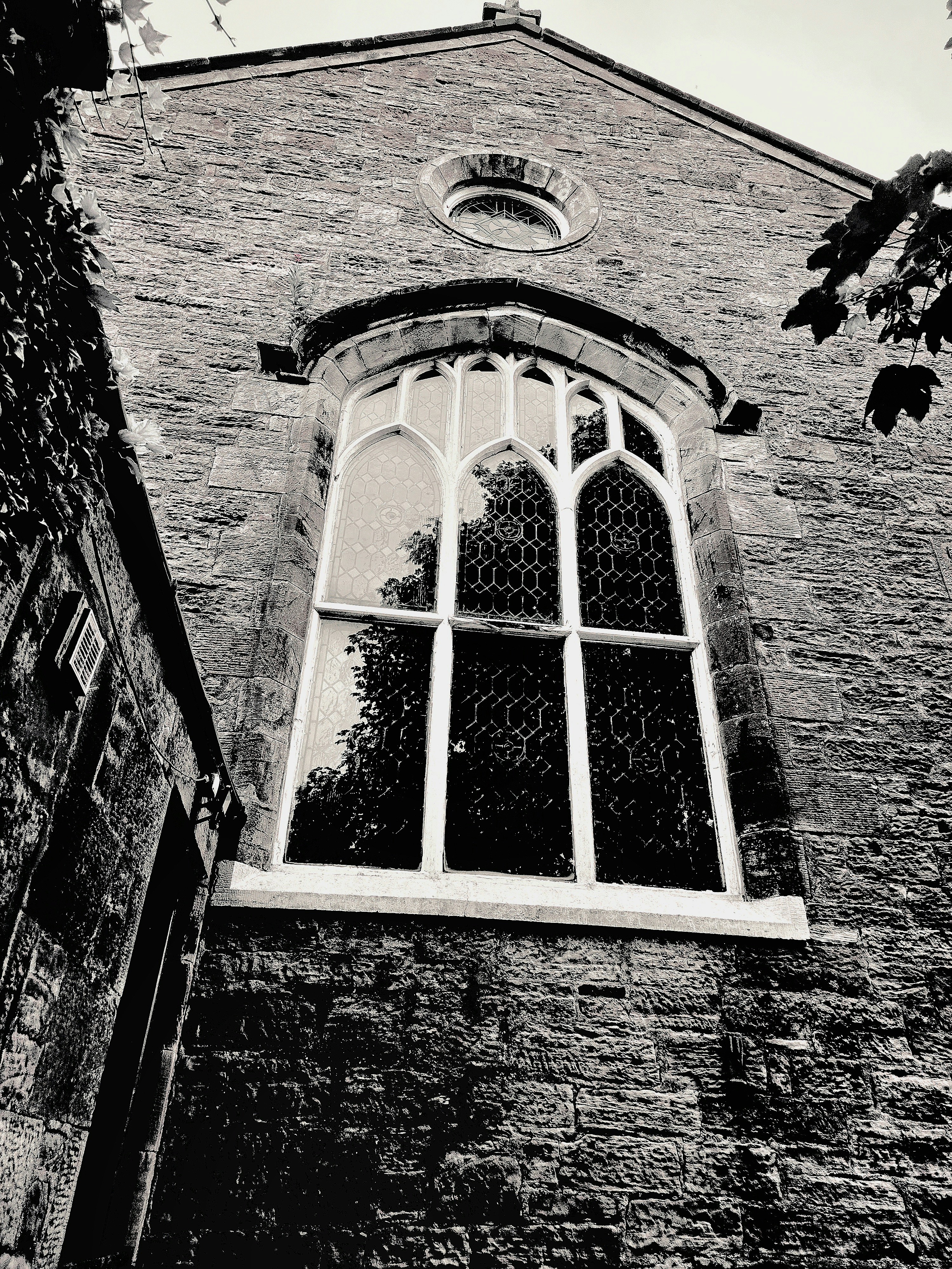 A tall arched window with leaded glass on a textured stone church wall