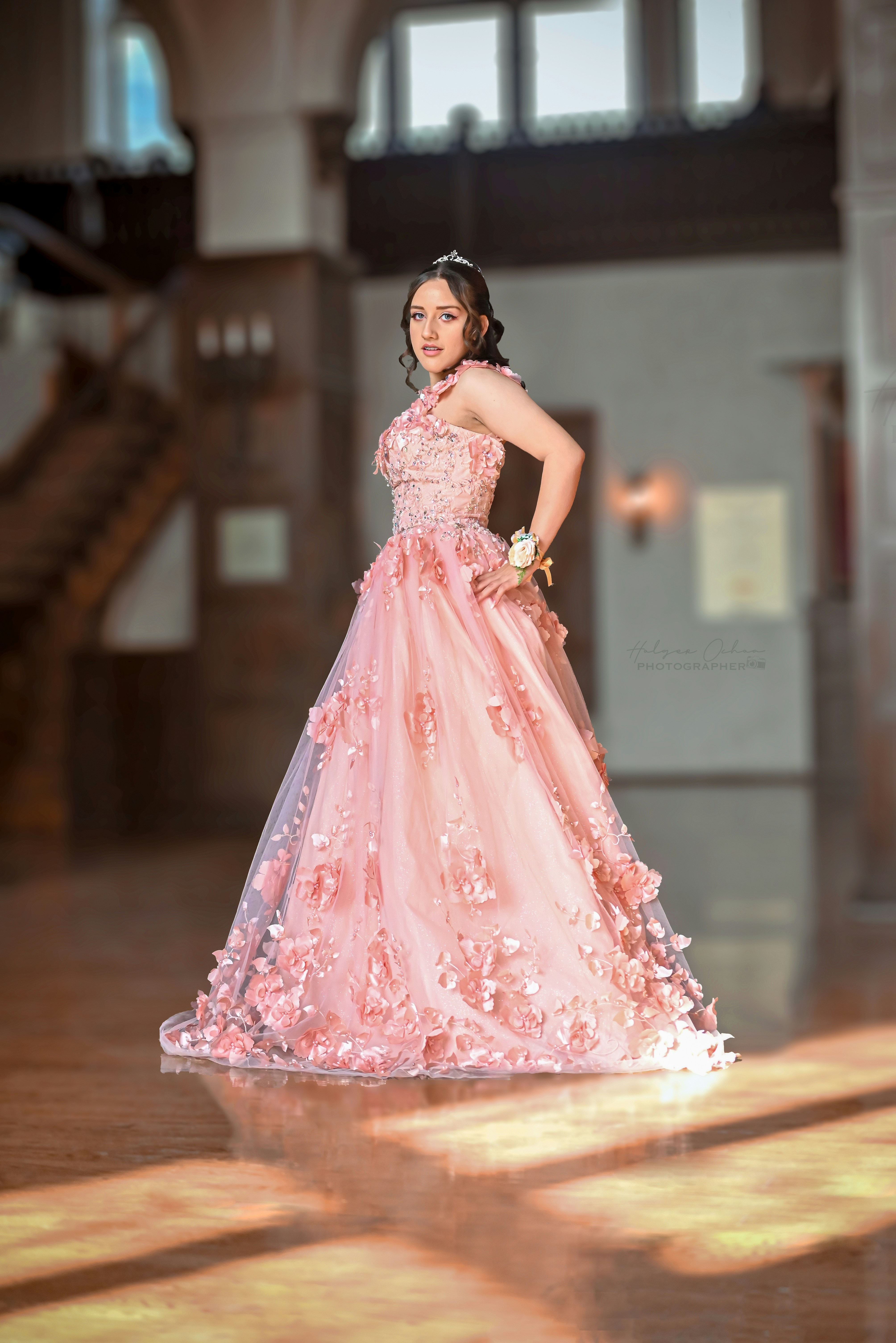 A young woman in a pink floral ball gown wearing a tiara in a hall