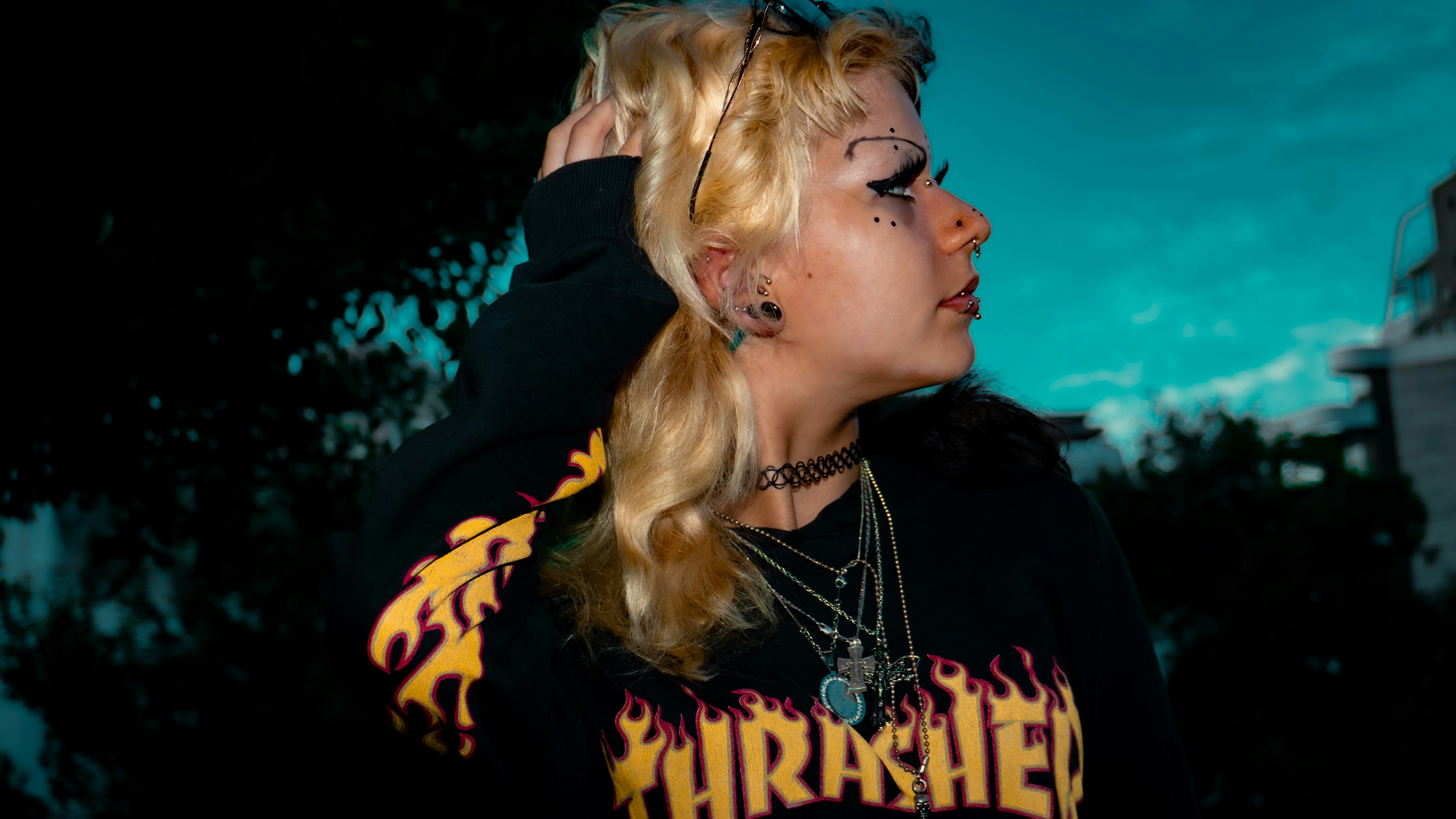 A person with blonde hair and facial piercings wearing a black flame print sweatshirt