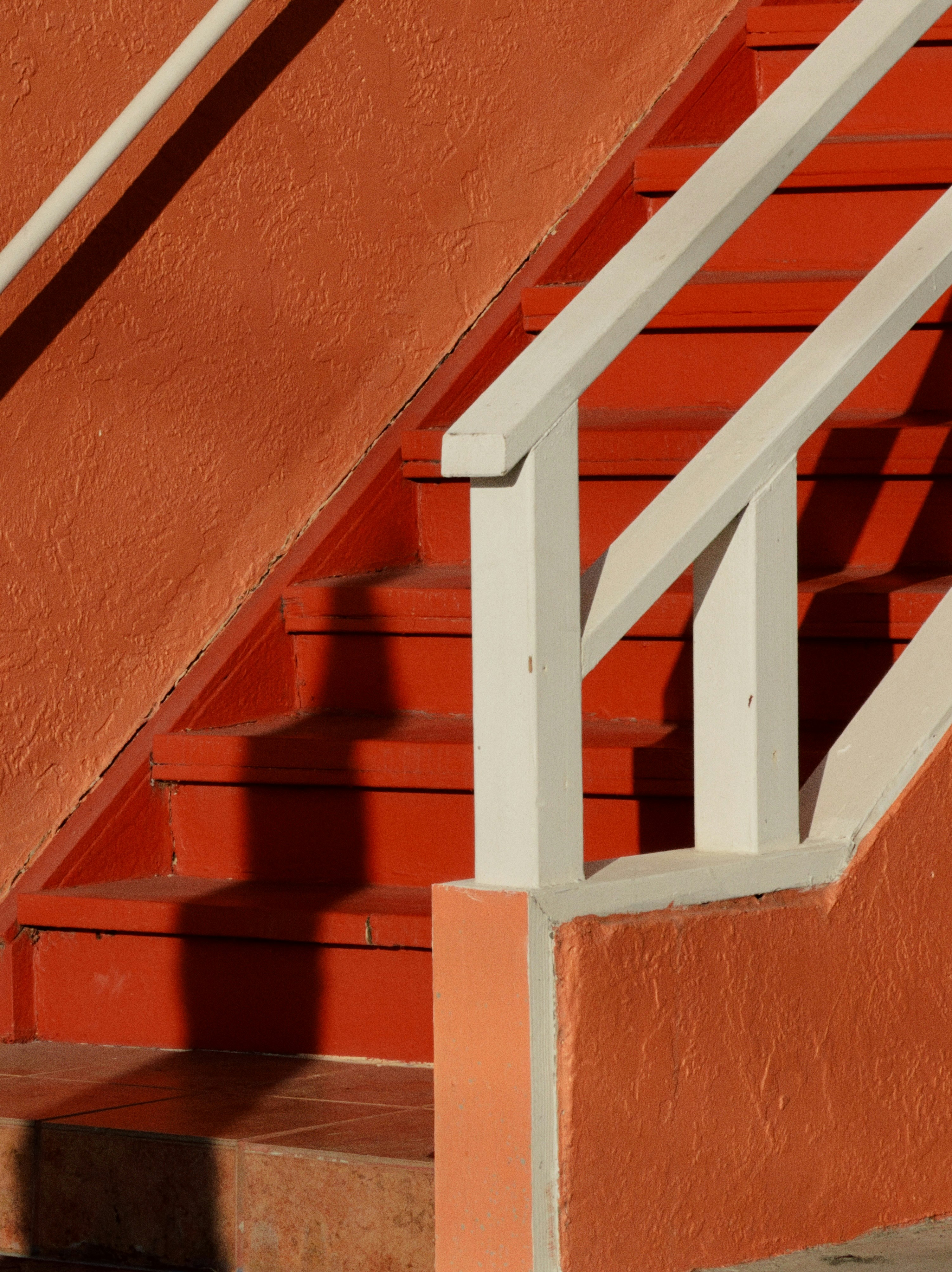 Escaliers extérieurs orange vif avec rampes blanches projetant de longues ombres au soleil