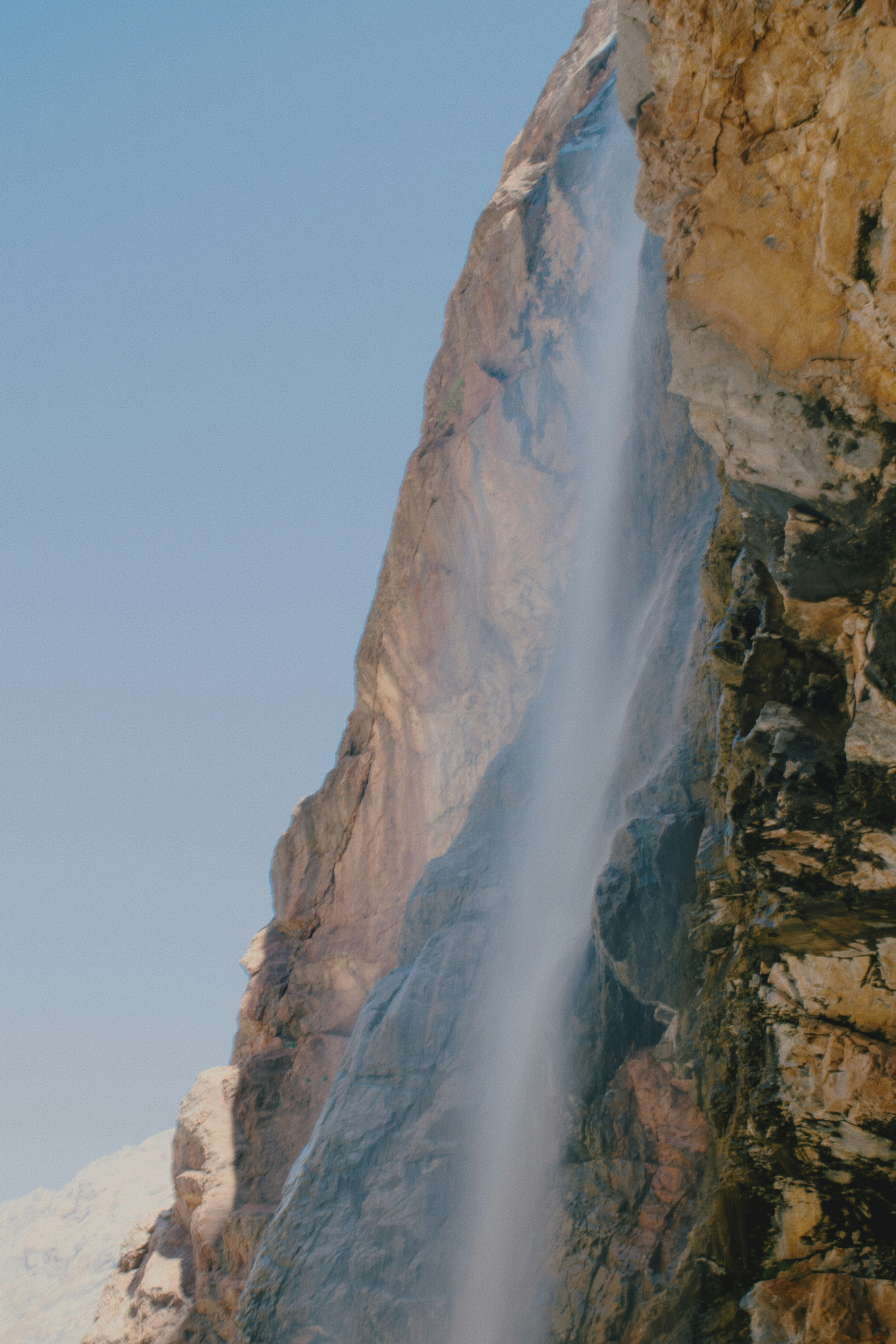 A thin waterfall cascading down a steep and textured rocky cliff face