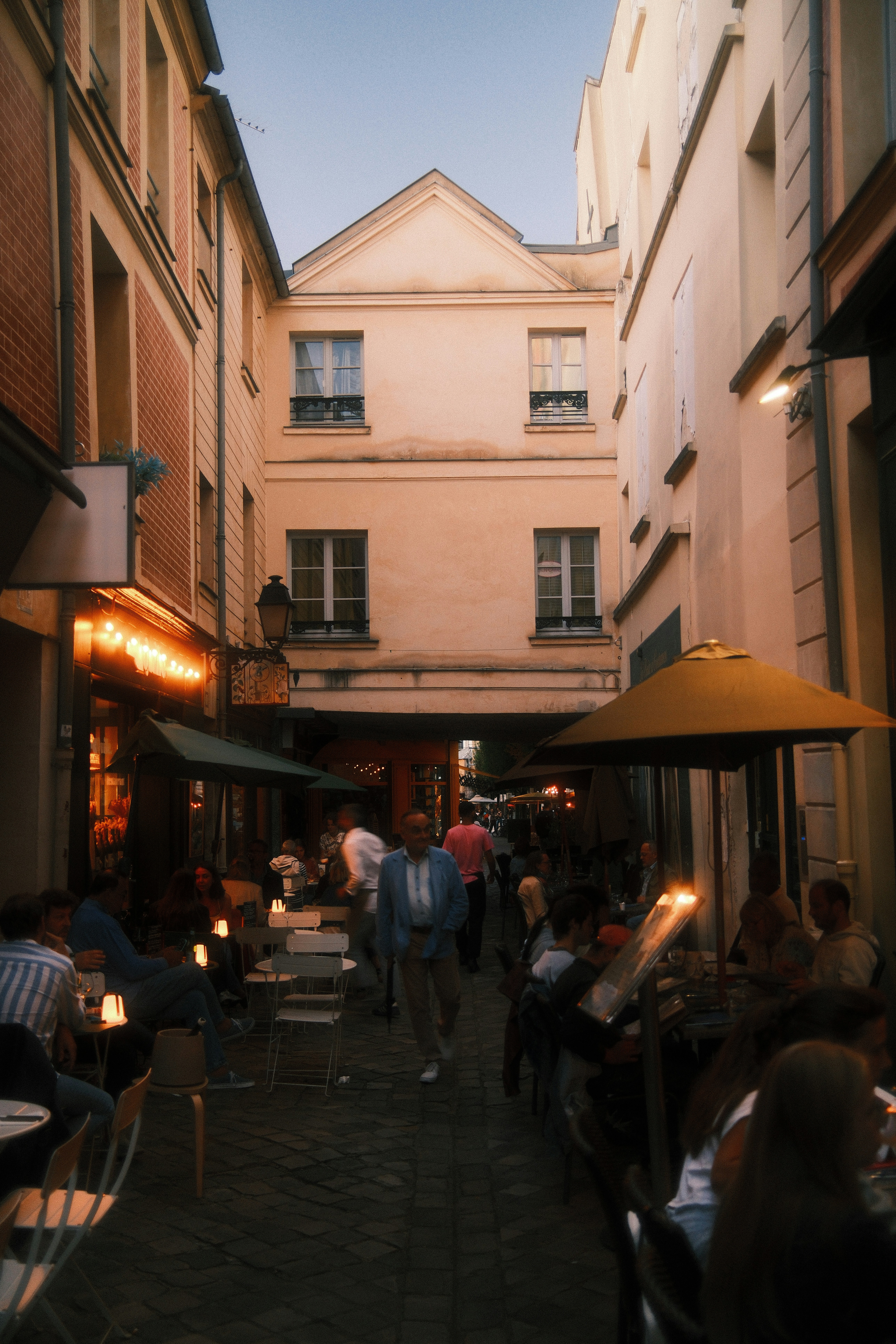People dining at outdoor tables in a narrow cobblestone alleyway in Paris