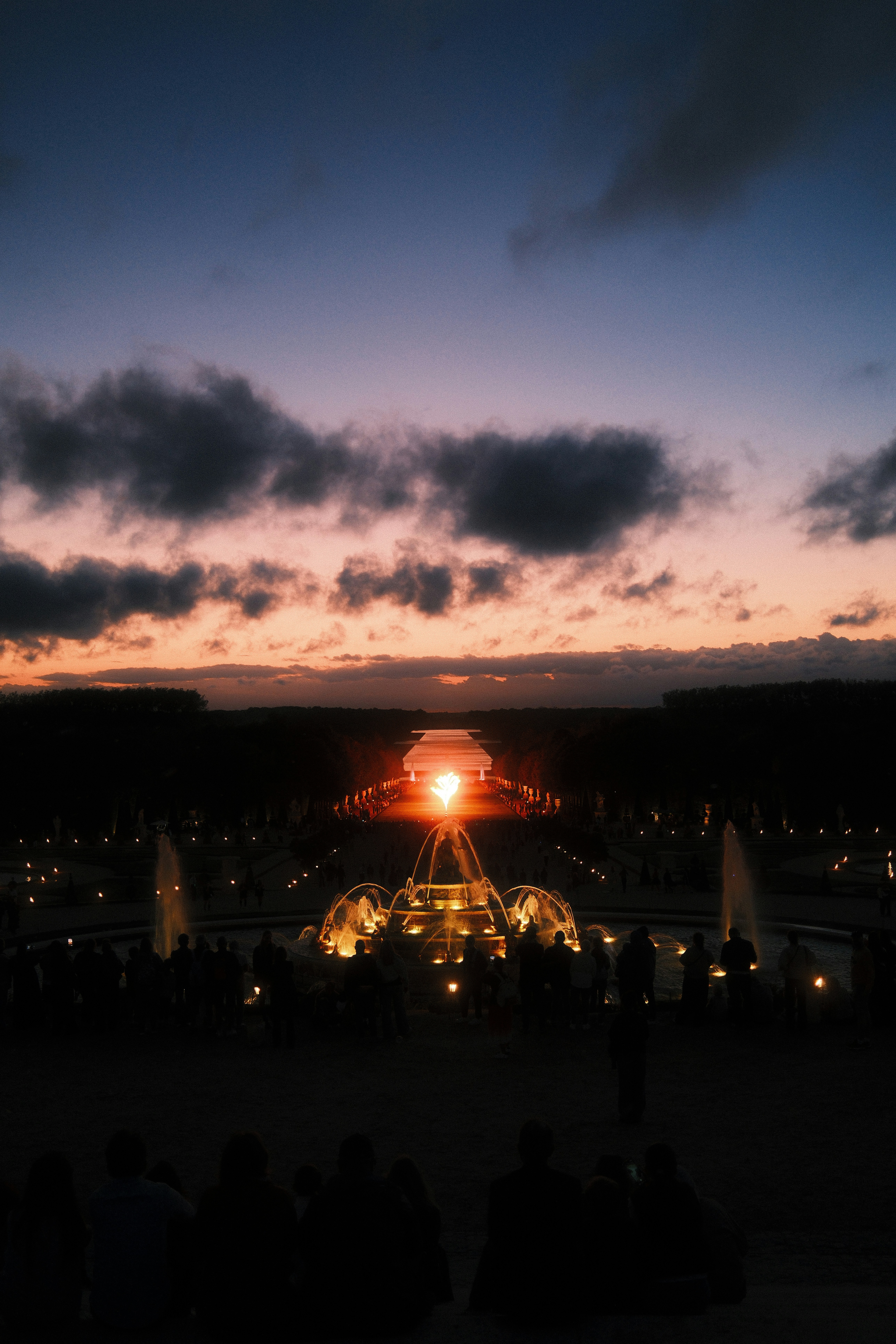 A crowd of people watching a glowing fountain in the Palace of Versailles gardens