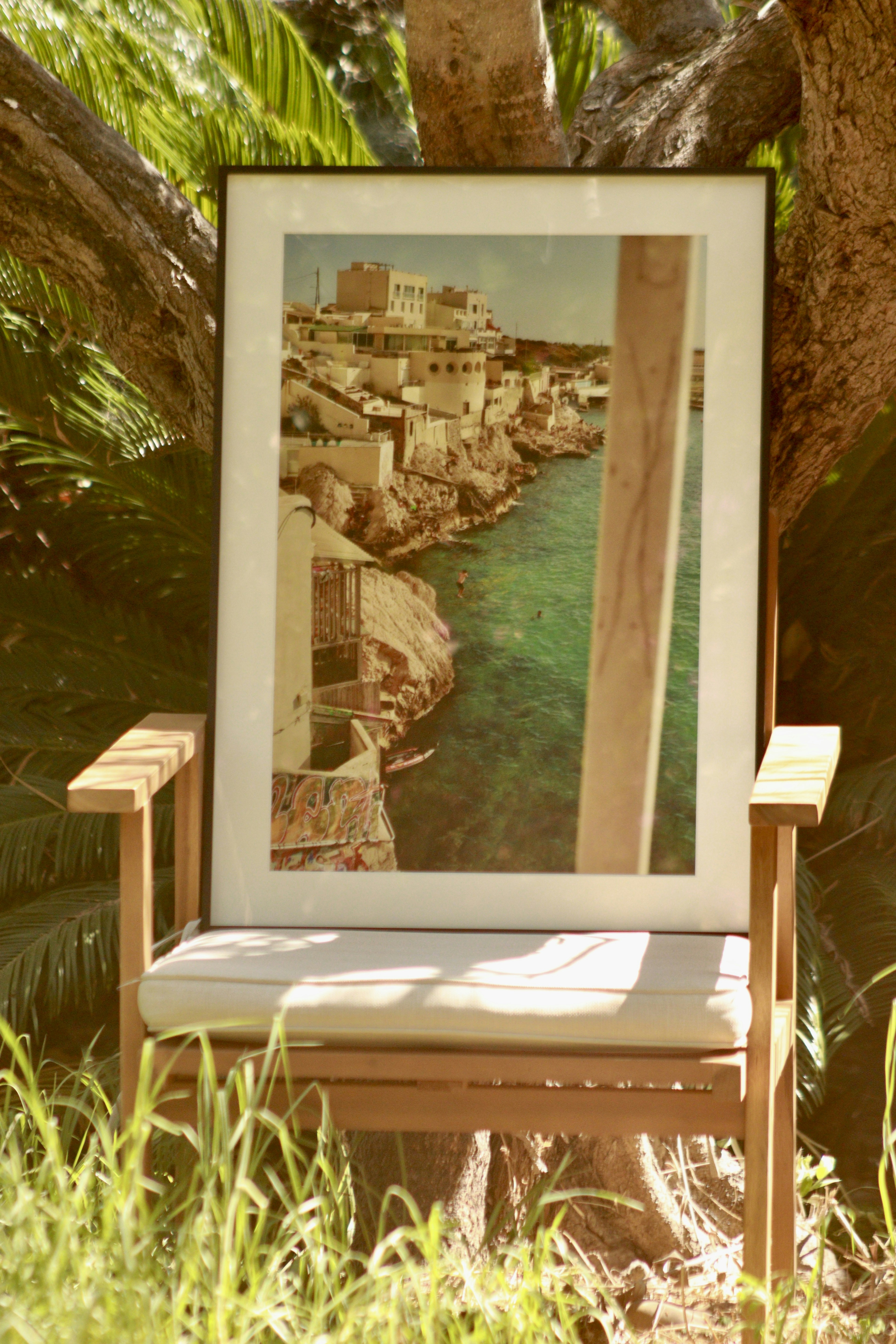 A framed photograph of a coastal town on a wooden chair outdoors