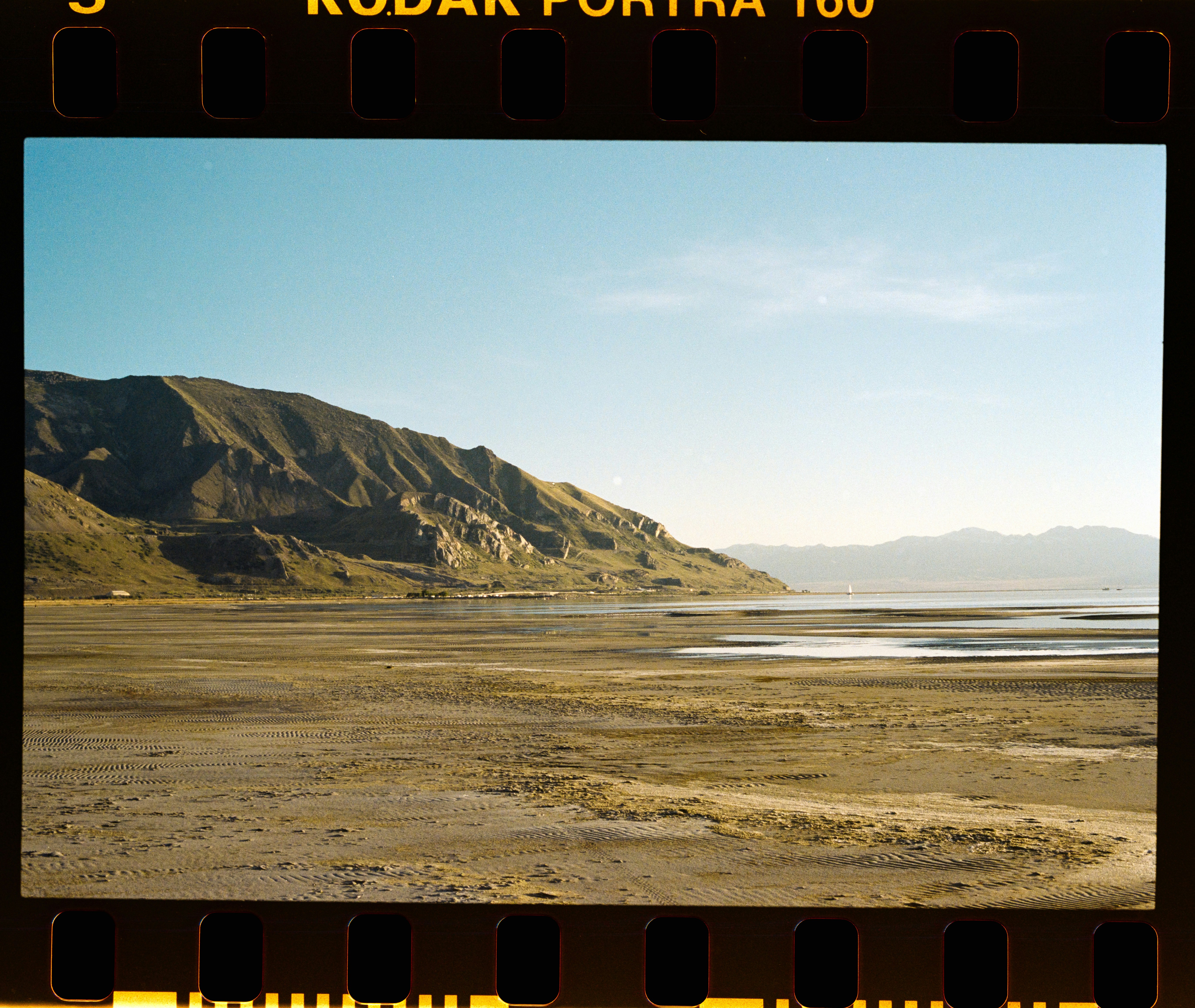 A vast mudflat stretching toward a mountain range under a clear blue sky