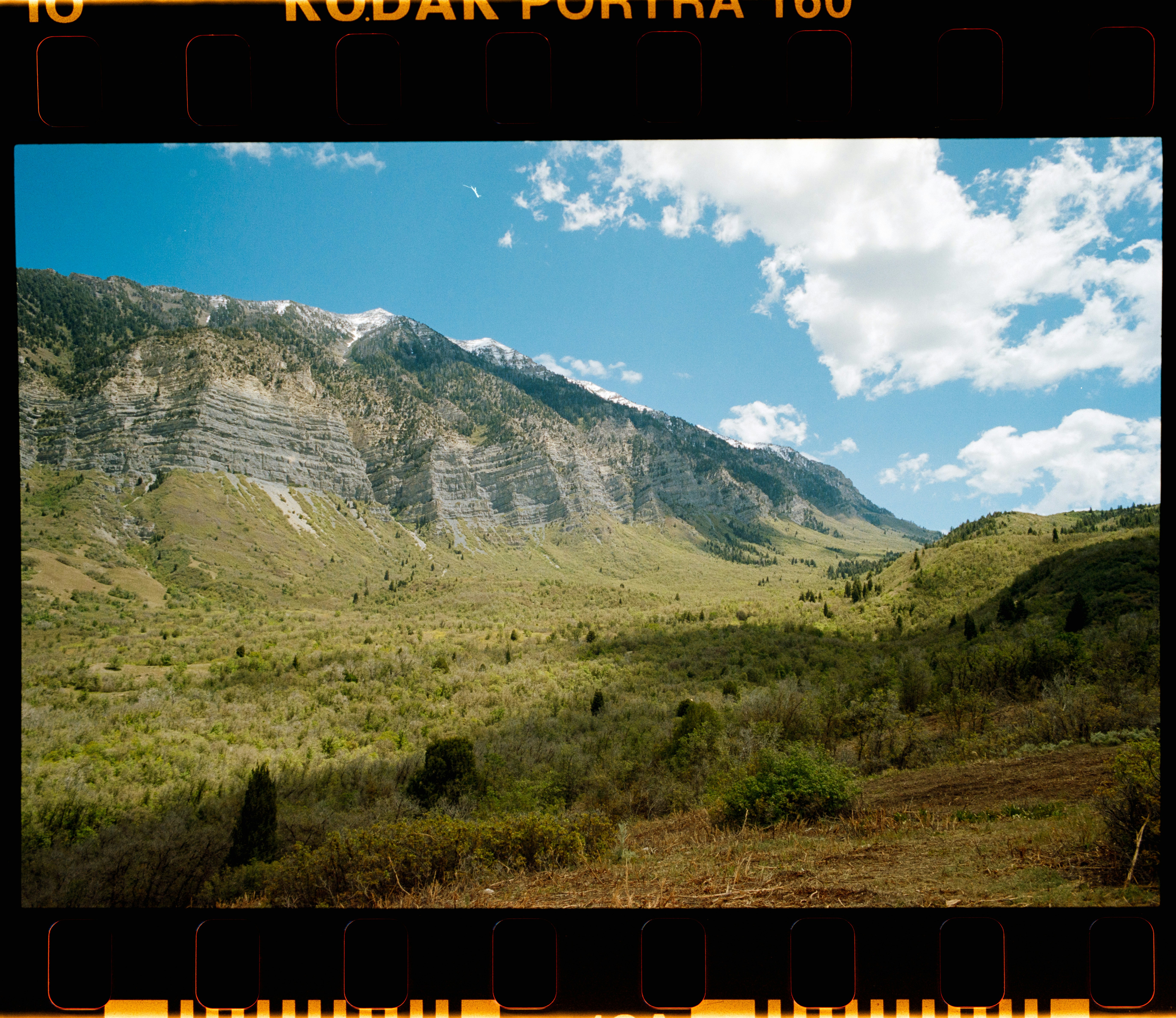 A steep mountain slope with rocky cliffs above a green valley under blue sky