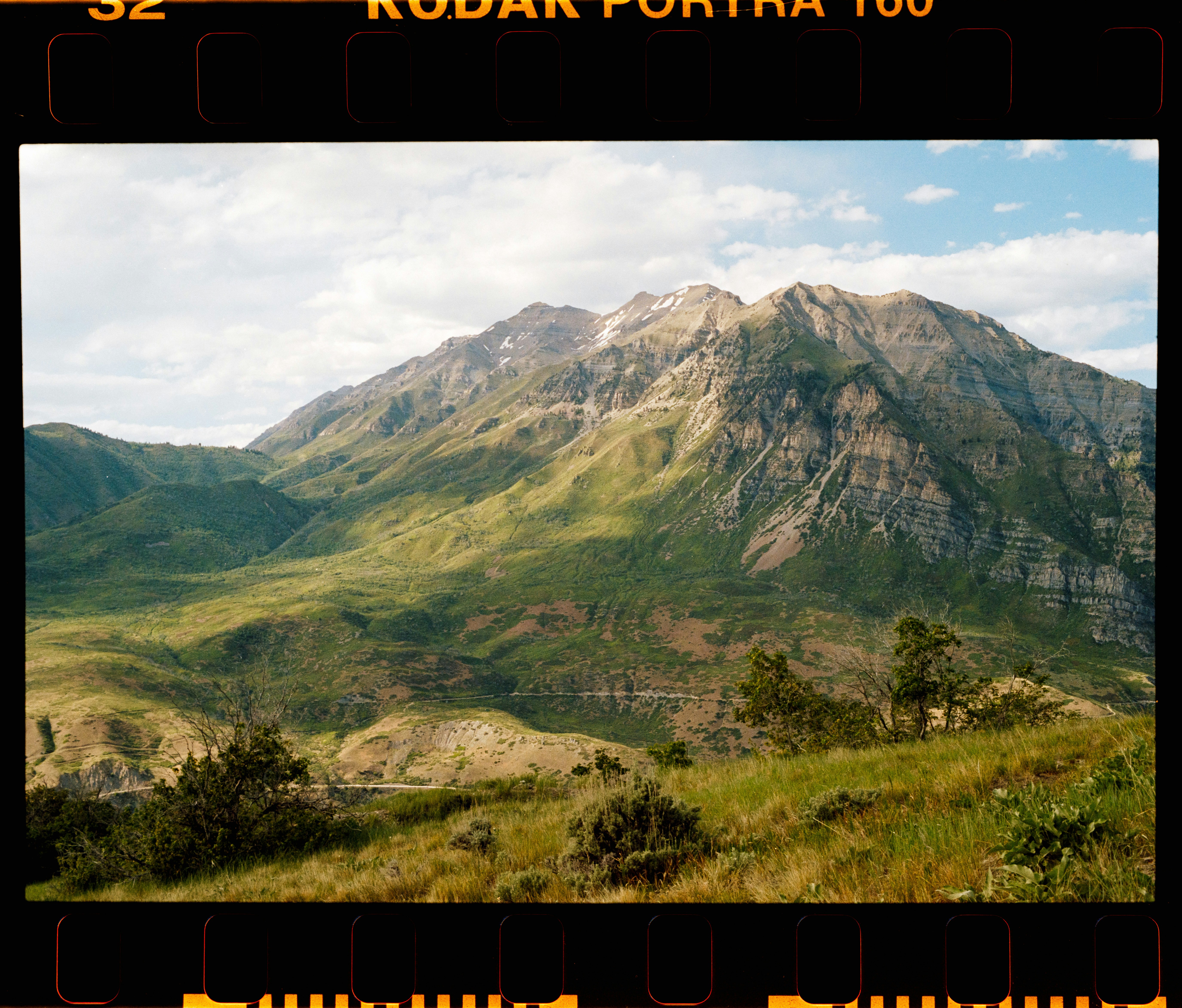 A rugged mountain range with green slopes and rocky peaks under a cloudy sky