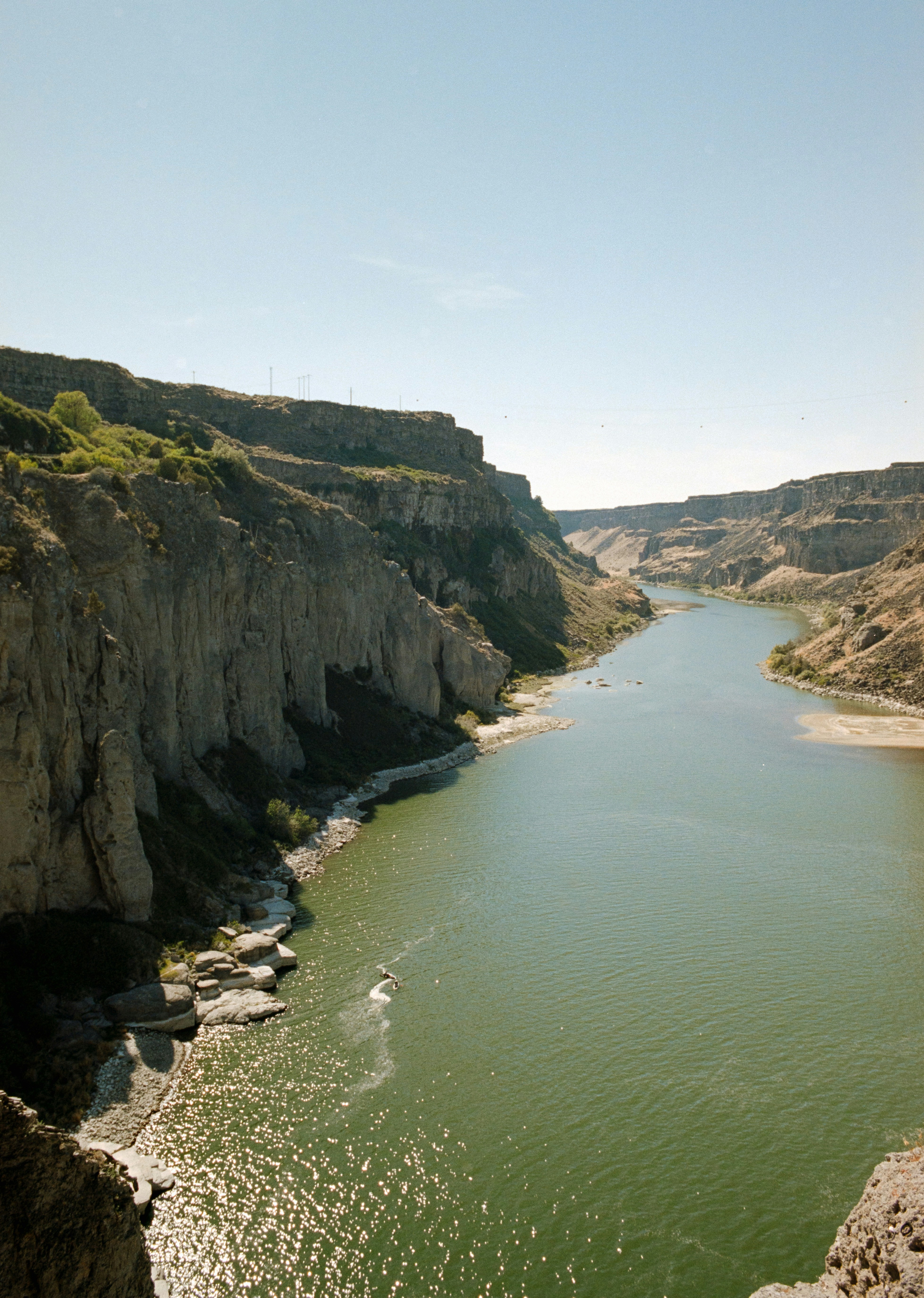 A river flowing through a deep canyon with steep rocky cliffs under clear skies