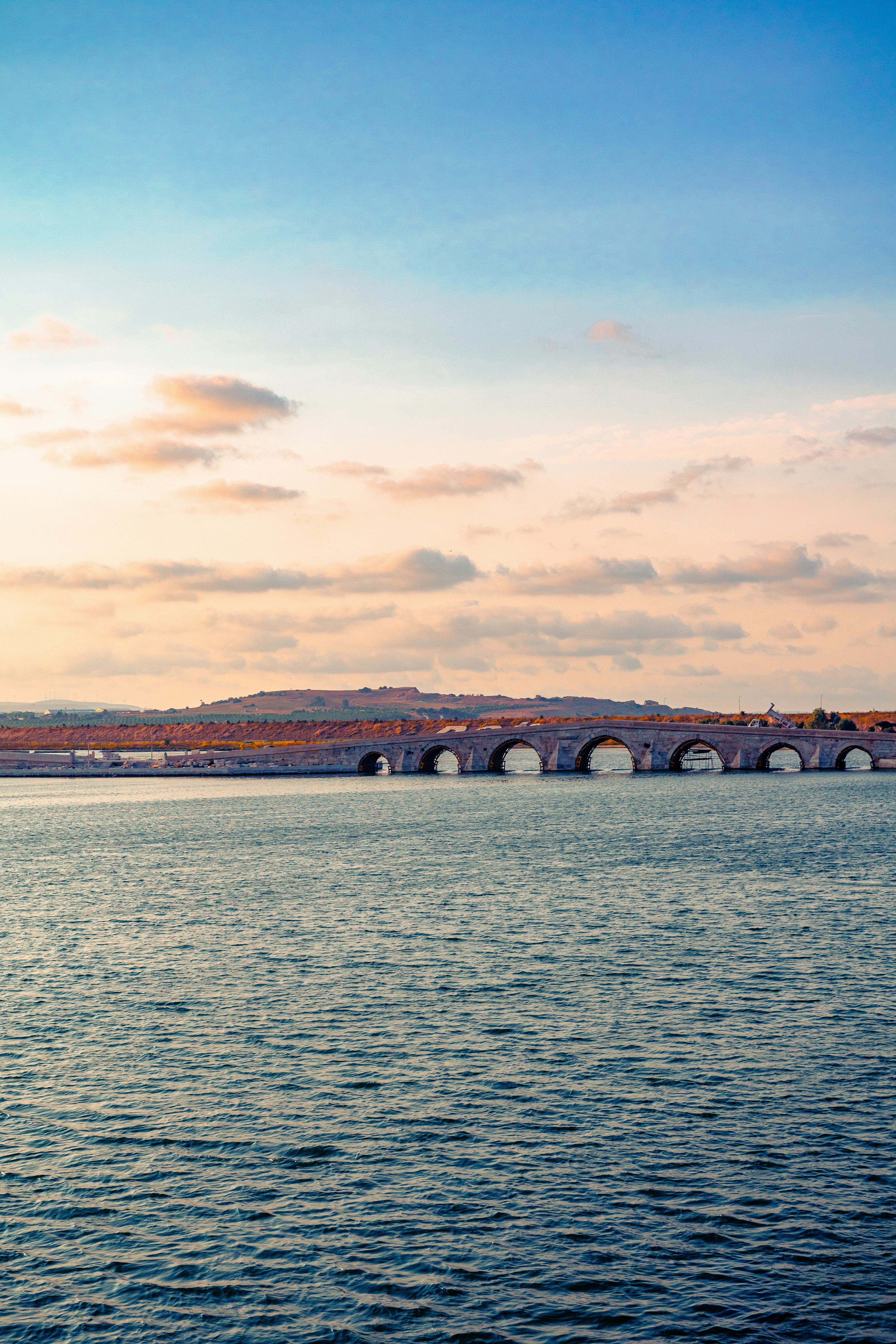 A long stone bridge with multiple arches spanning across a calm body of water