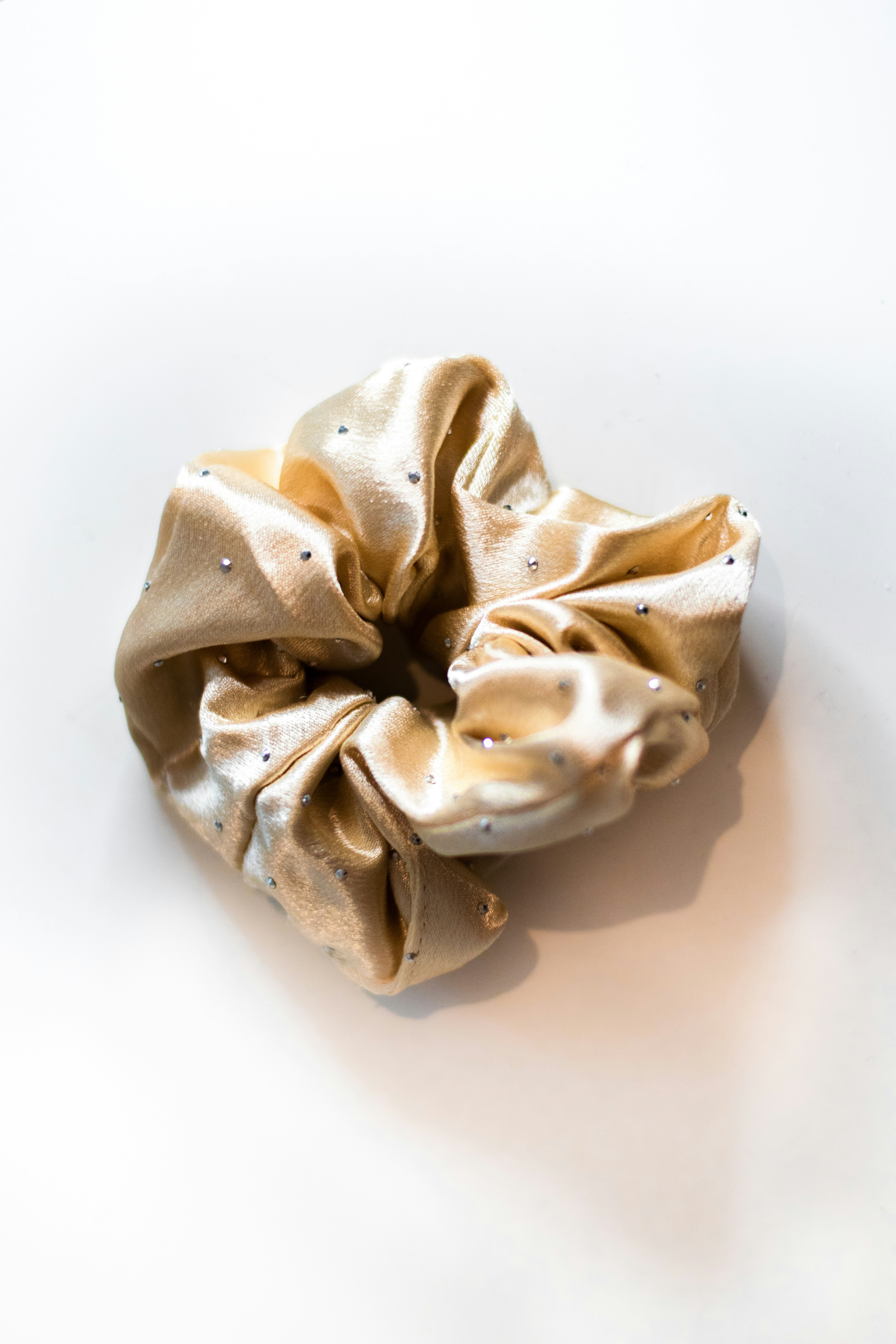 A gold satin scrunchie with small silver studs on a white surface