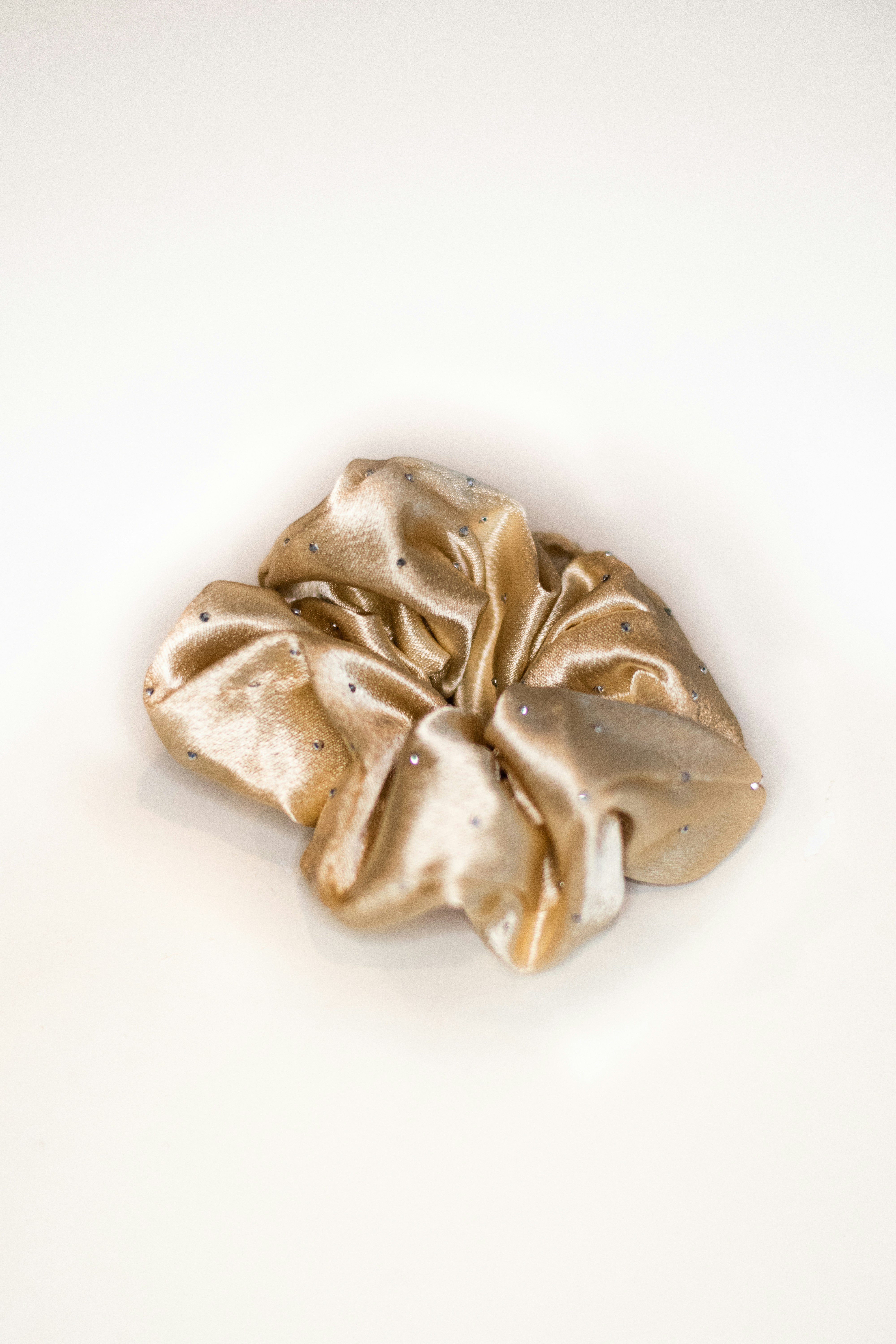 A gold satin hair scrunchie with small embedded crystals on a white surface