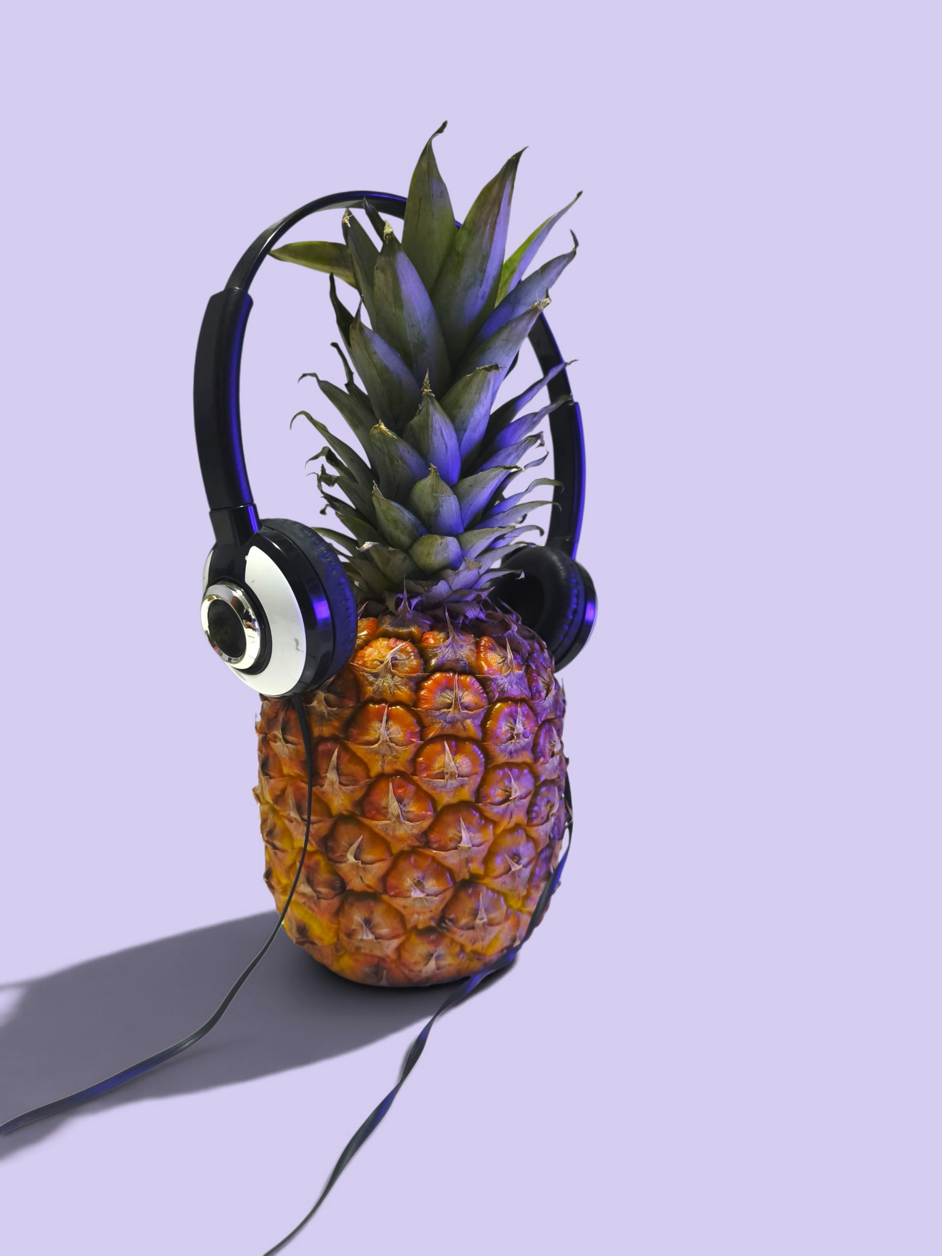 A pineapple wearing black headphones against a solid light purple background