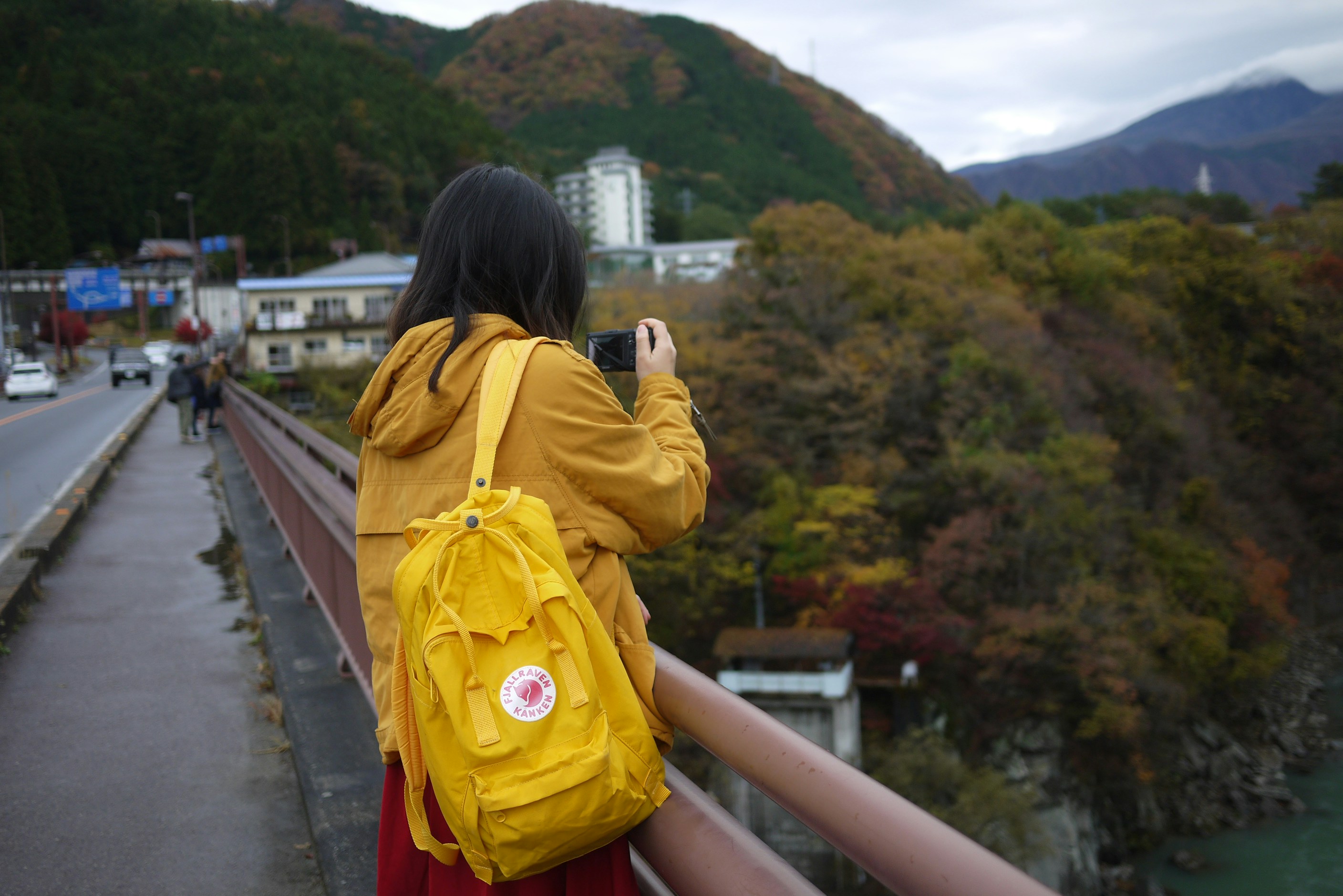 A person with a yellow backpack taking a photo from a bridge in autumn